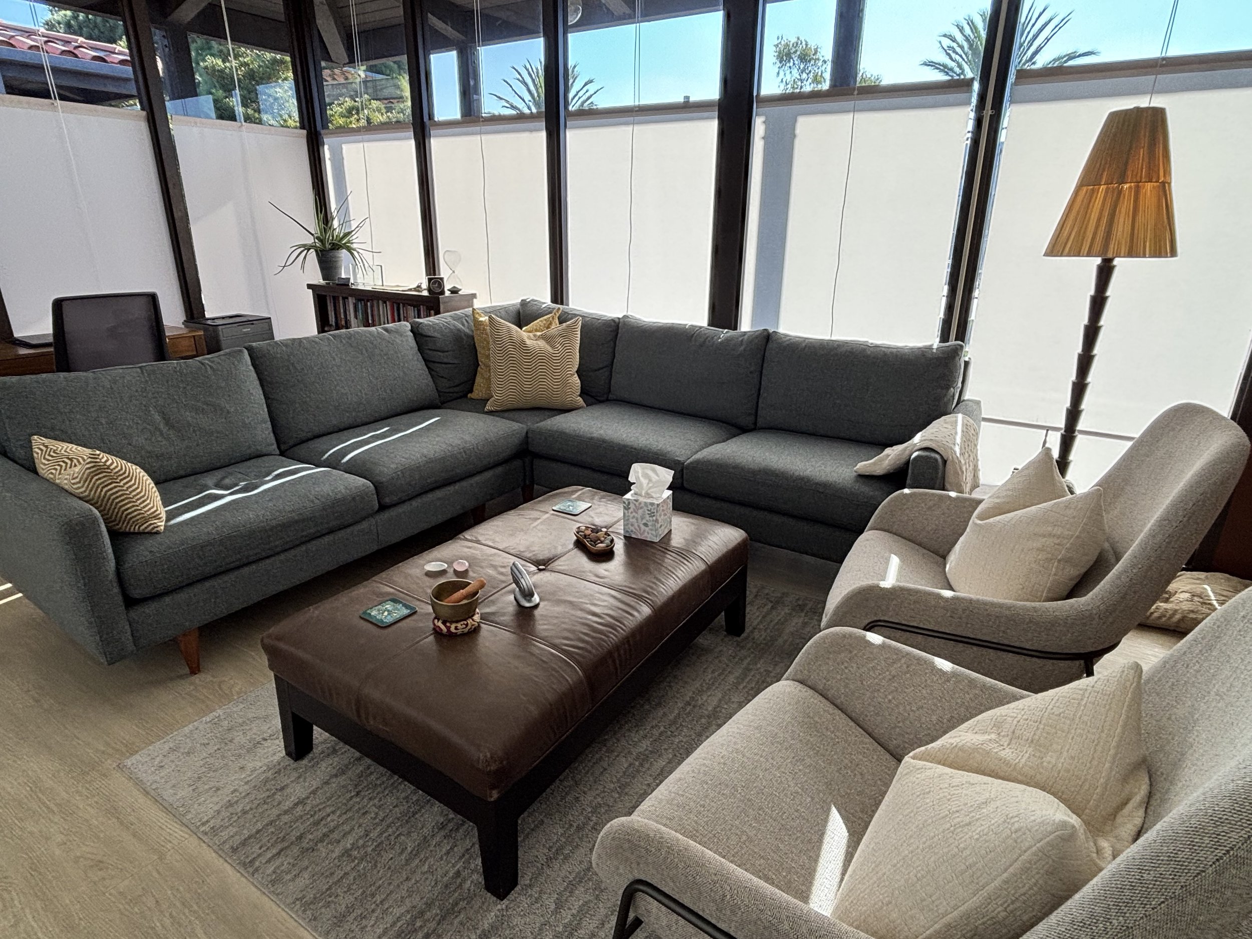 Therapy office in Santa Monica  sectional sofa, armchairs, a brown leather ottoman, a tall lamp, large windows.