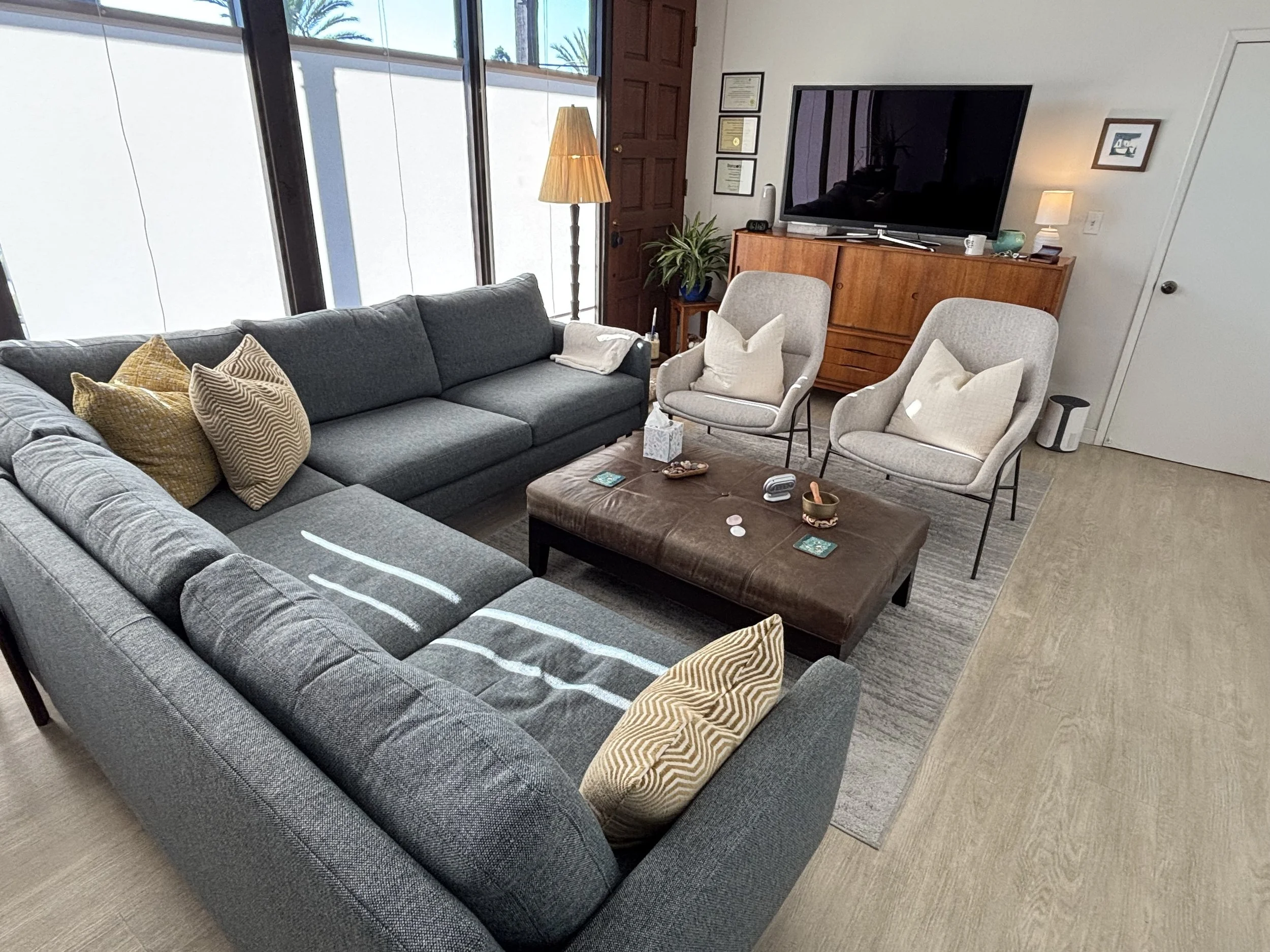 Therapy office in Santa Monica with a large sectional sofa, two armchairs, a leather ottoman and windows letting in natural light.