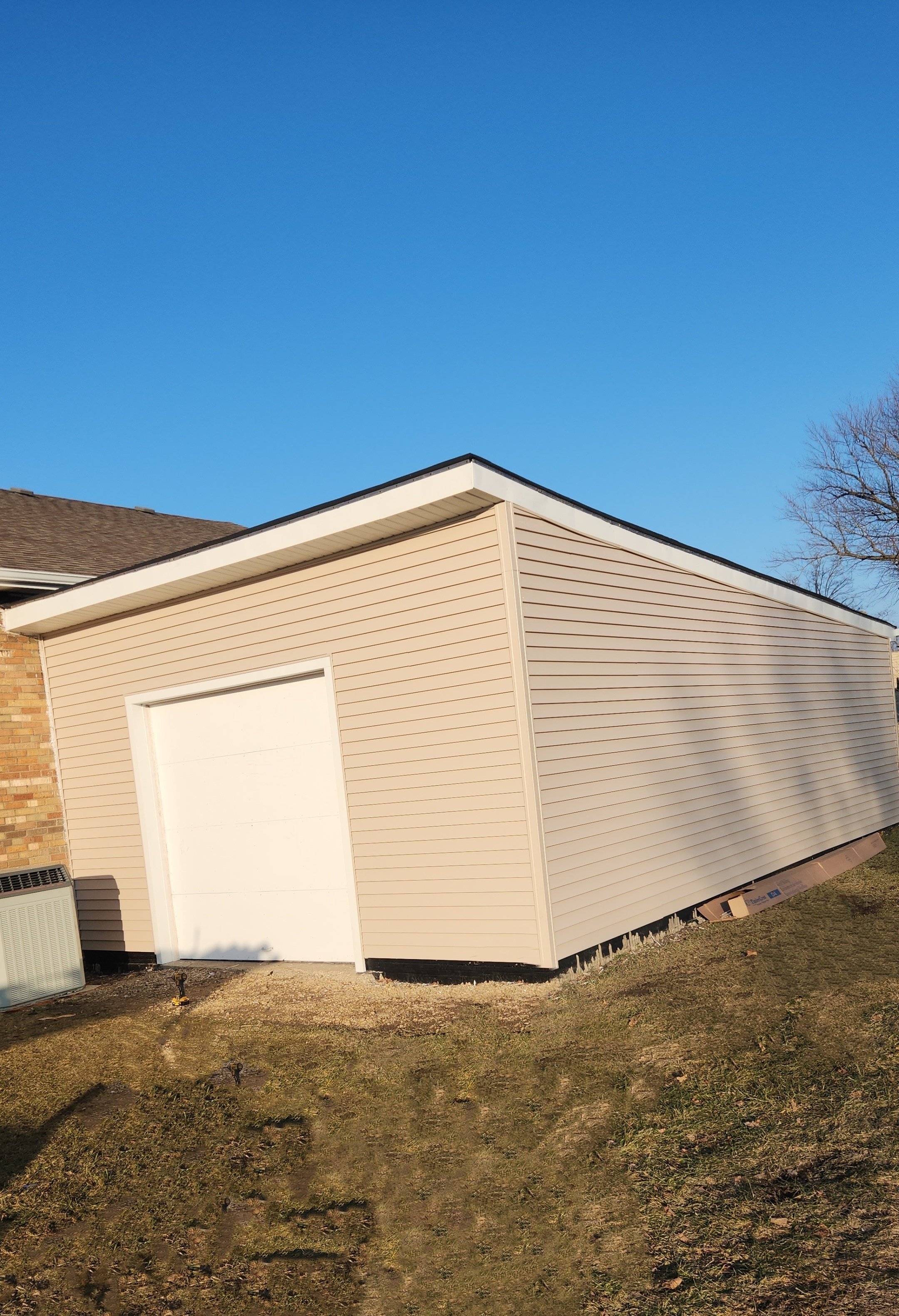 Beige detached garage with white door and sloped roof 