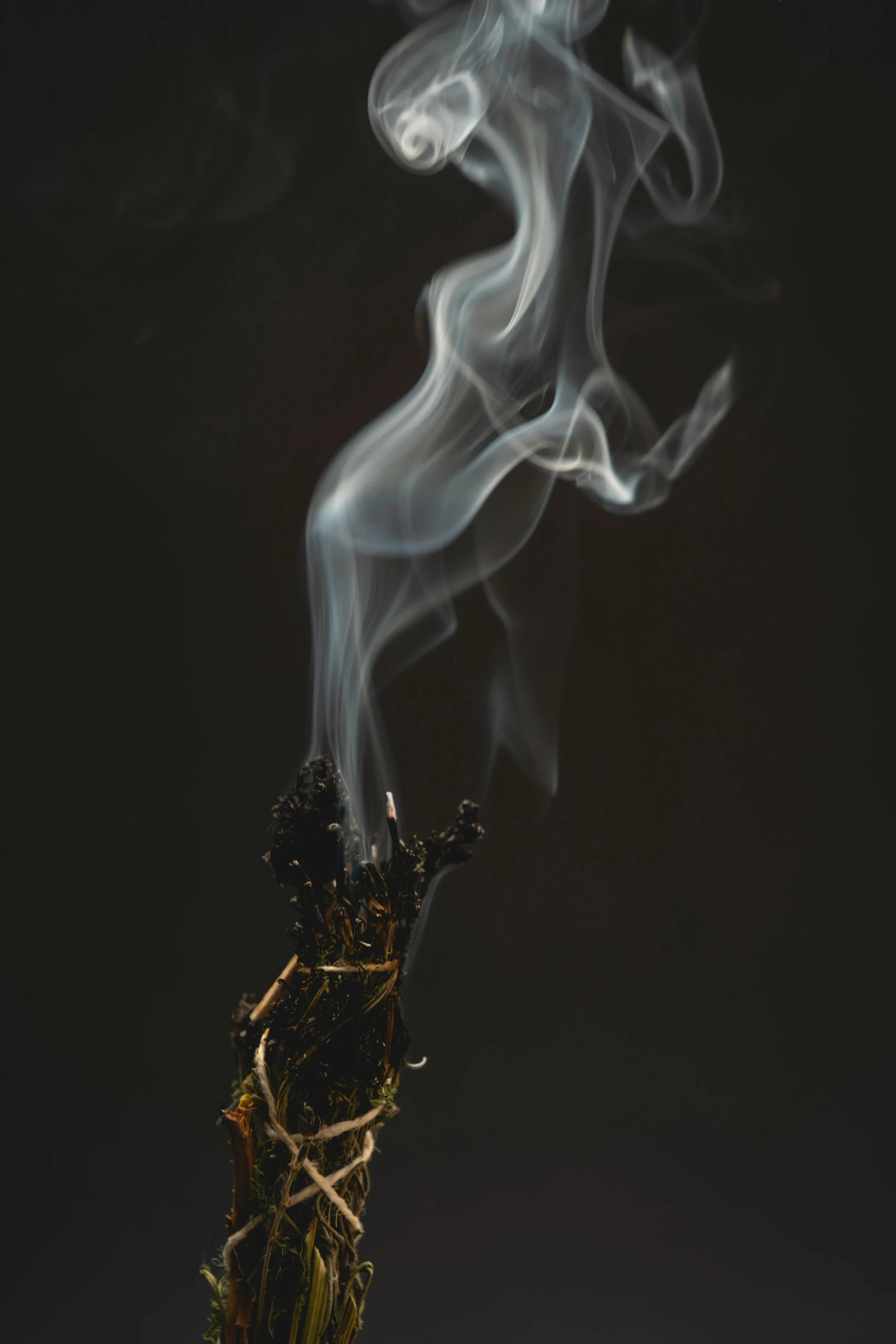A smoking smudge bundle of herbs in twine