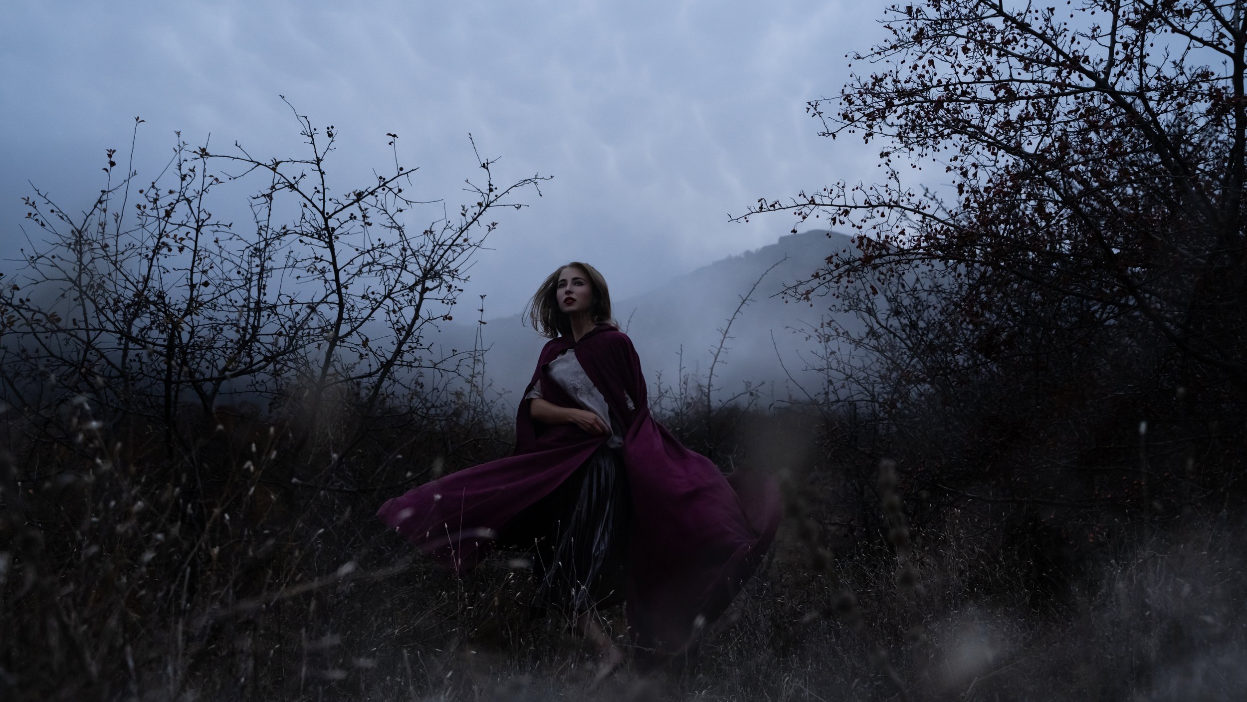 Woman on foggy hillside in a red hooded cloak