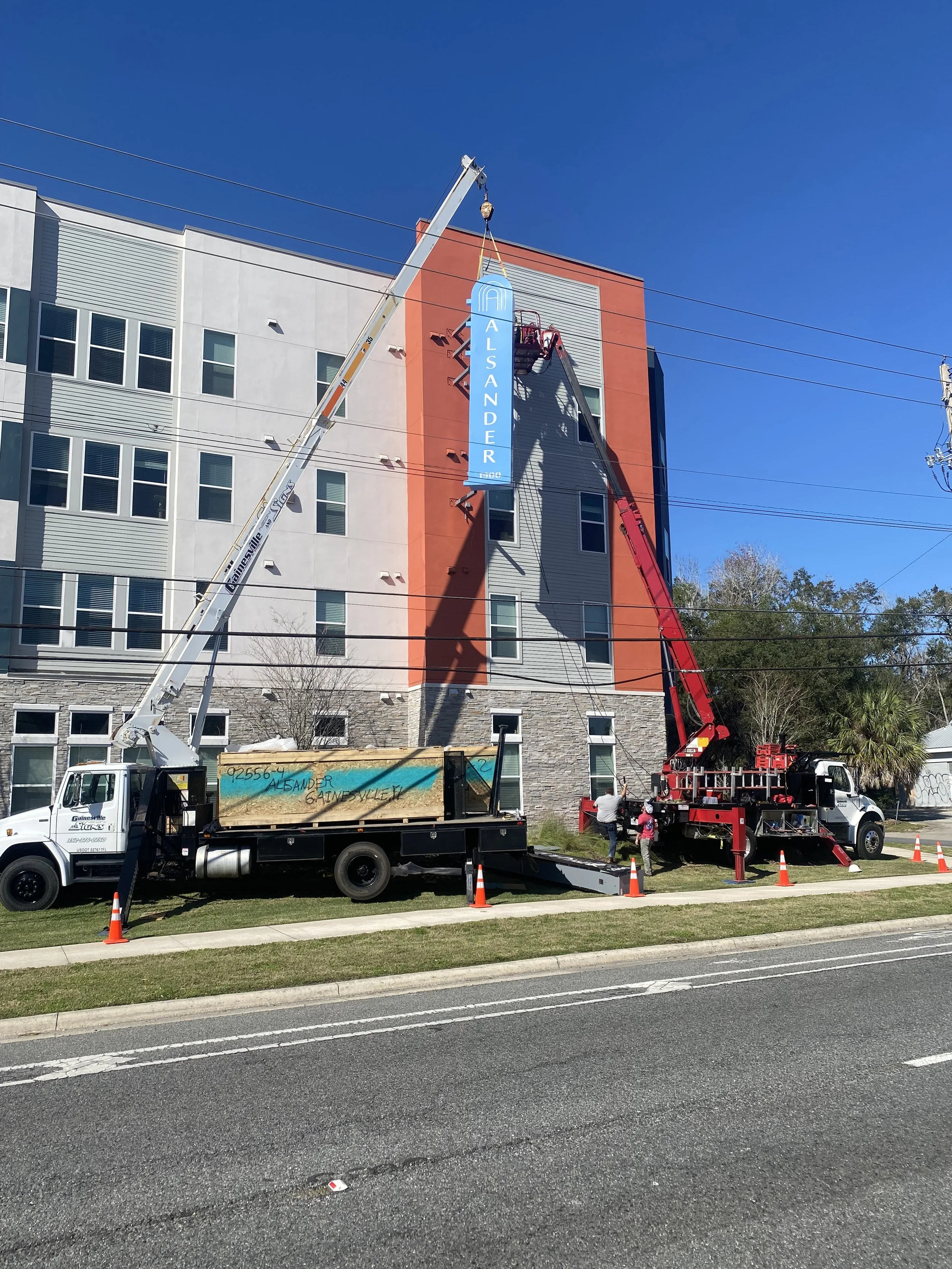 Lift truck installing an Alsander Apartments sign on the exterior of a building