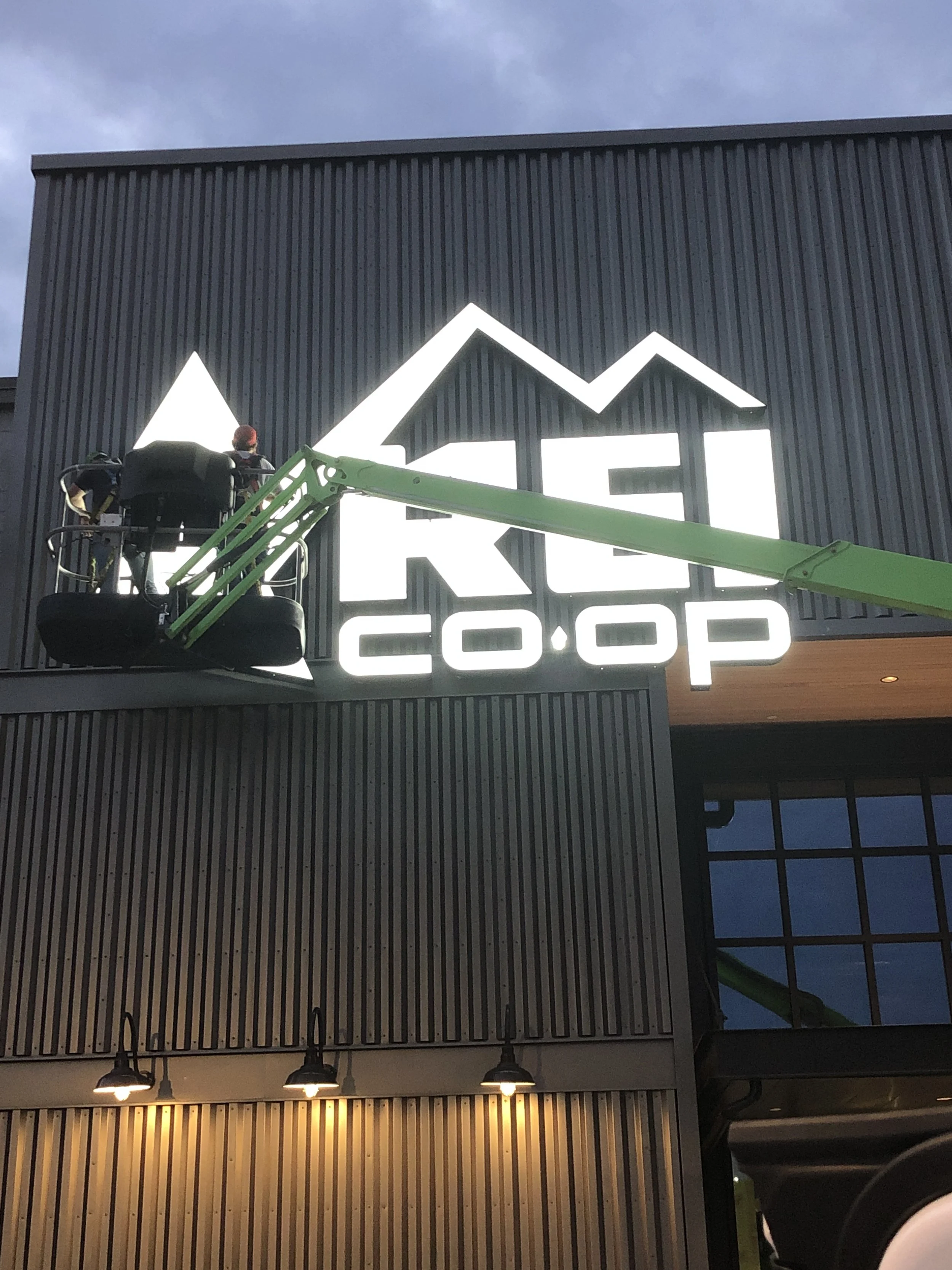 Man on a lift installing an REI Co-op sign on the exterior of a building