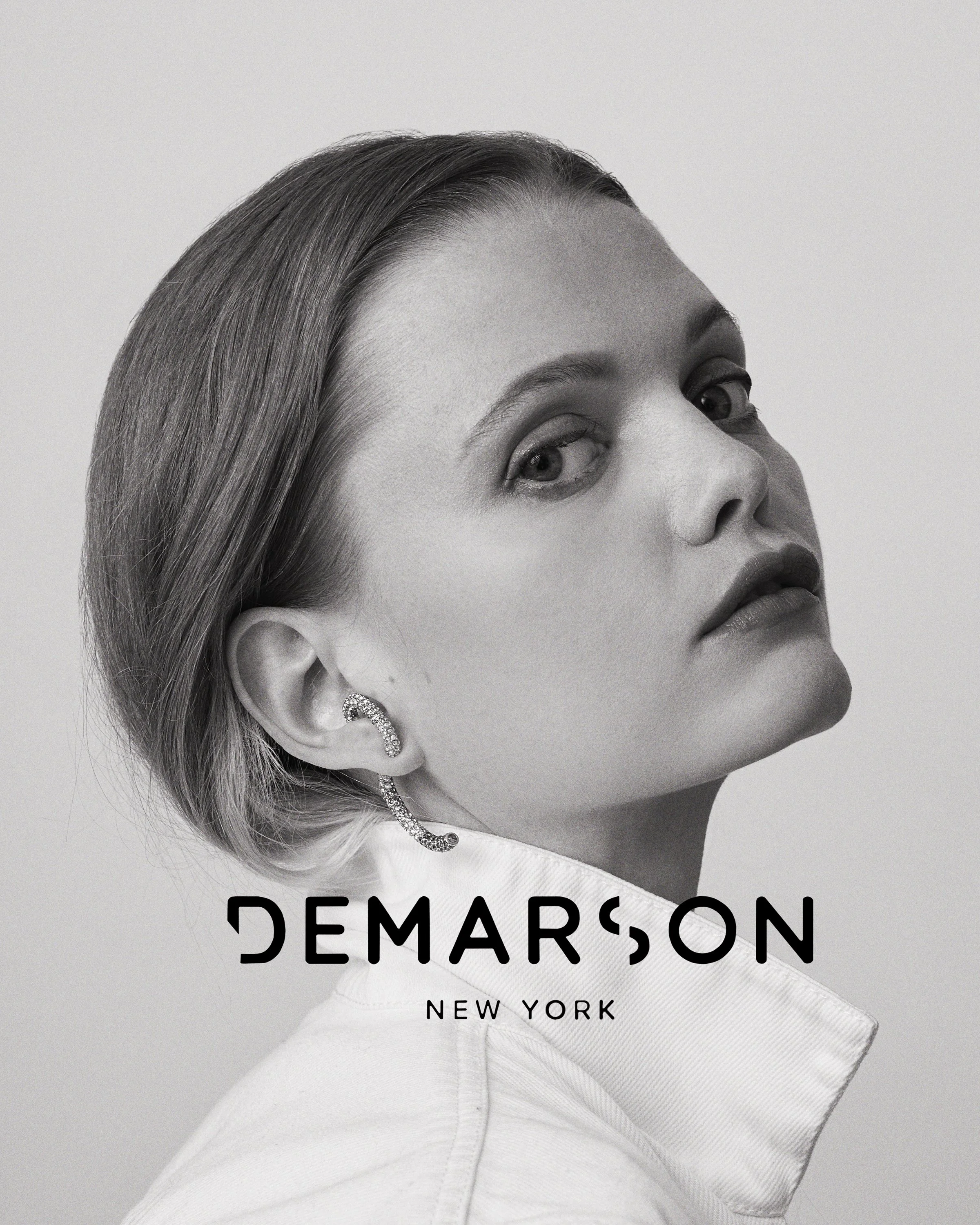 Black and white portrait of a woman with short hair, wearing an earring and a collared shirt, looking over her shoulder. The image features the text 'DEMARSON NEW YORK'.