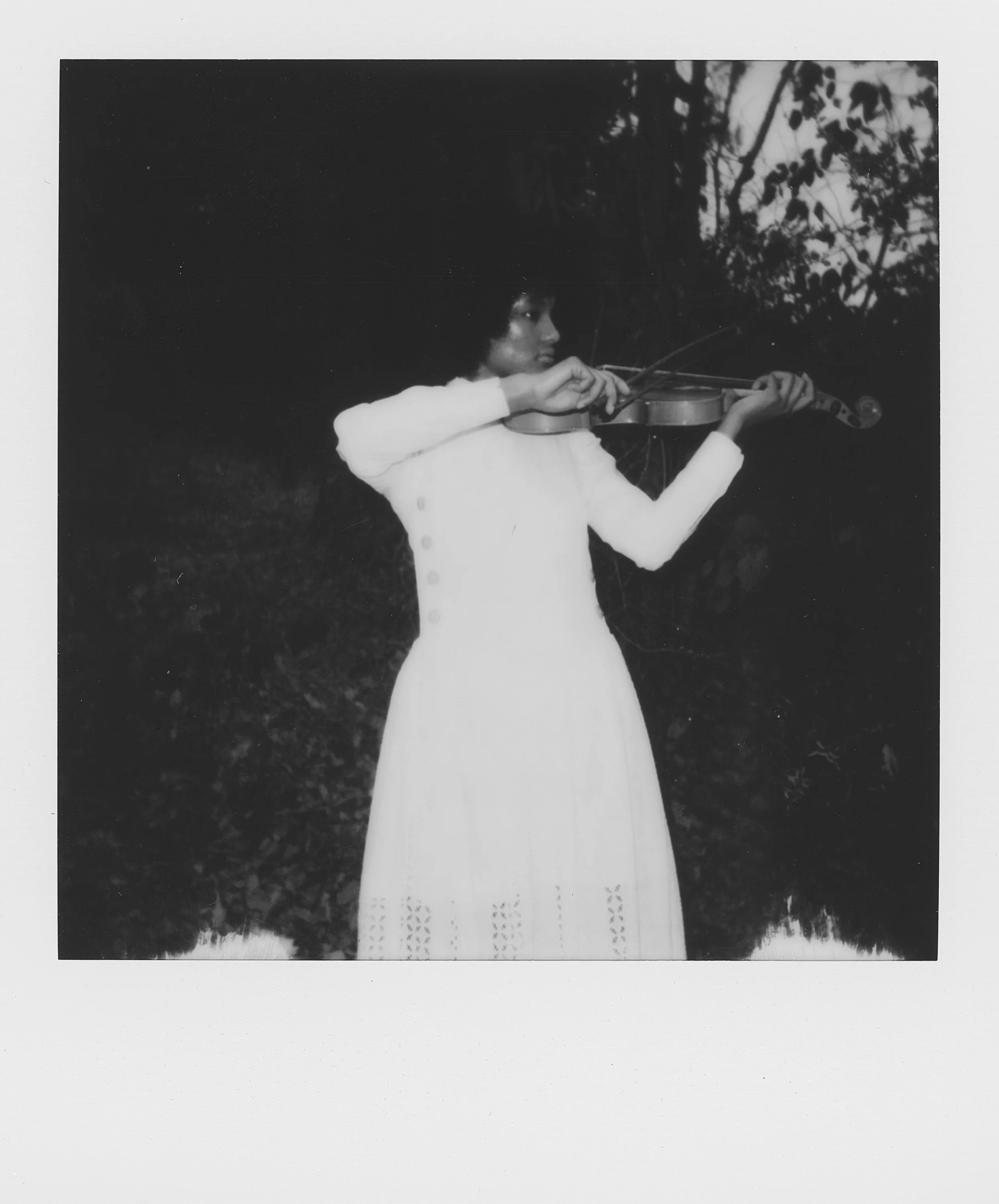 A woman wearing a white coat with buttons playing a violin outdoors.