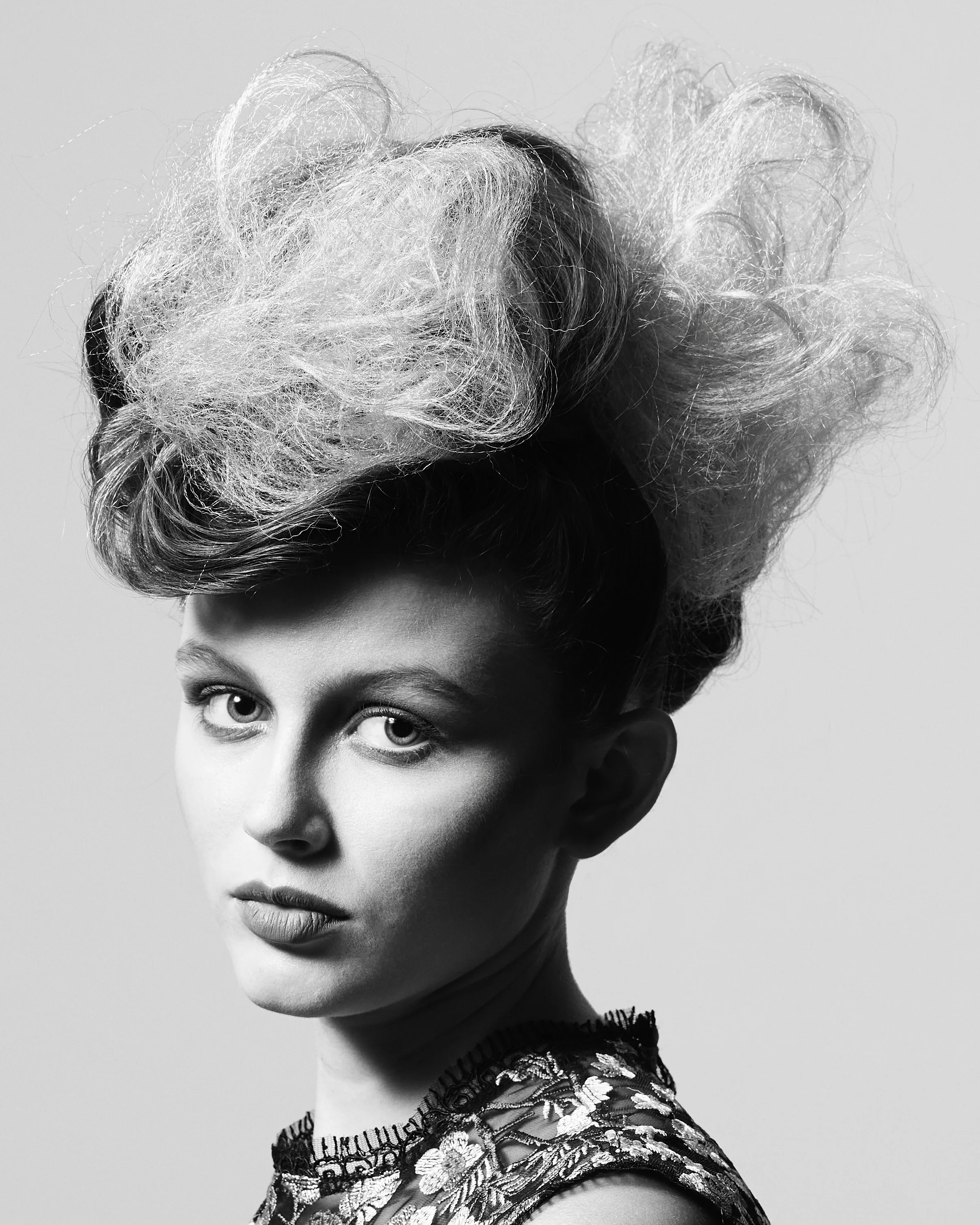 Black and white portrait of a woman with an elaborate, textured hairstyle and an embroidered top.