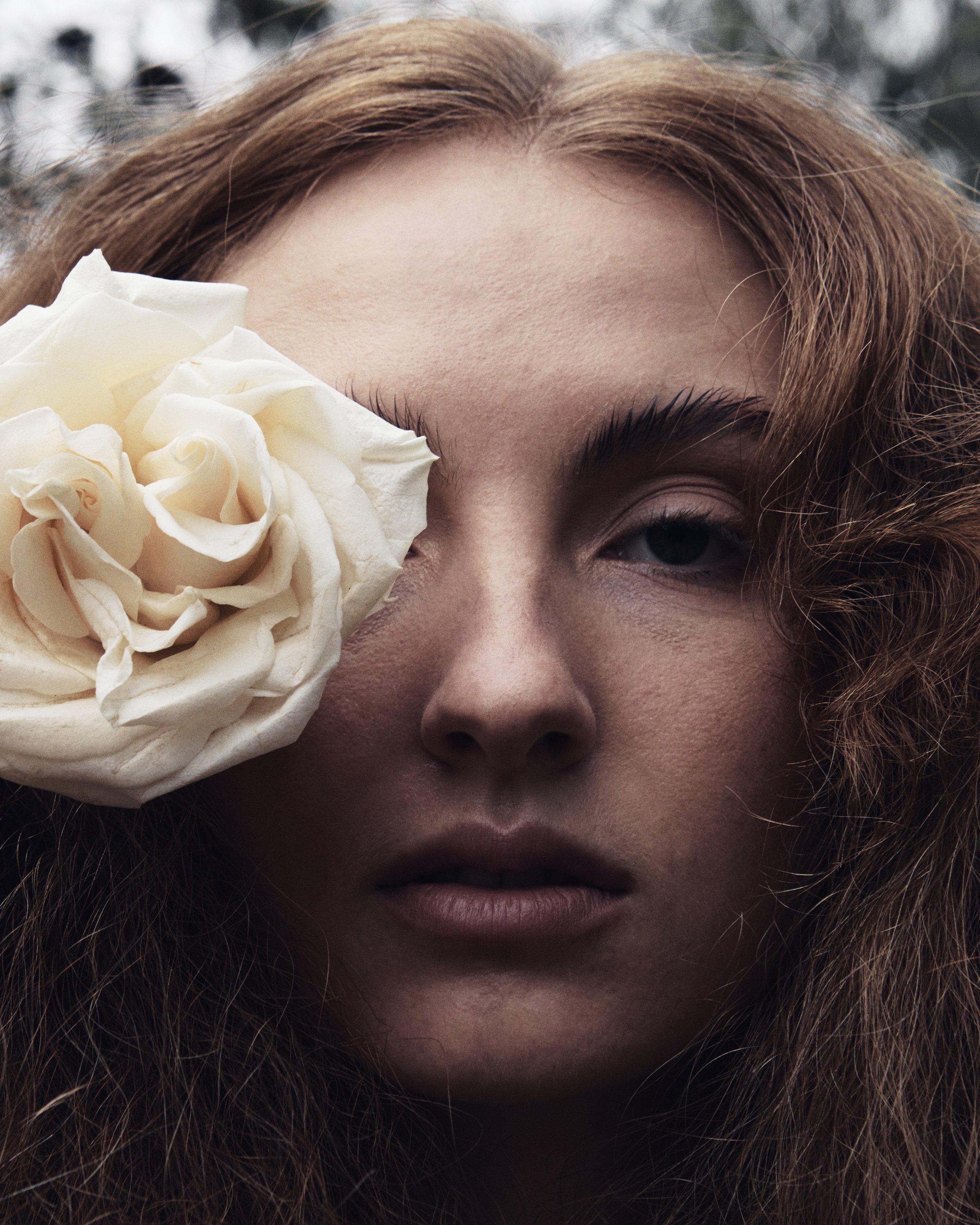 Close-up of a woman's face with an off-white rose covering part of her left eye.