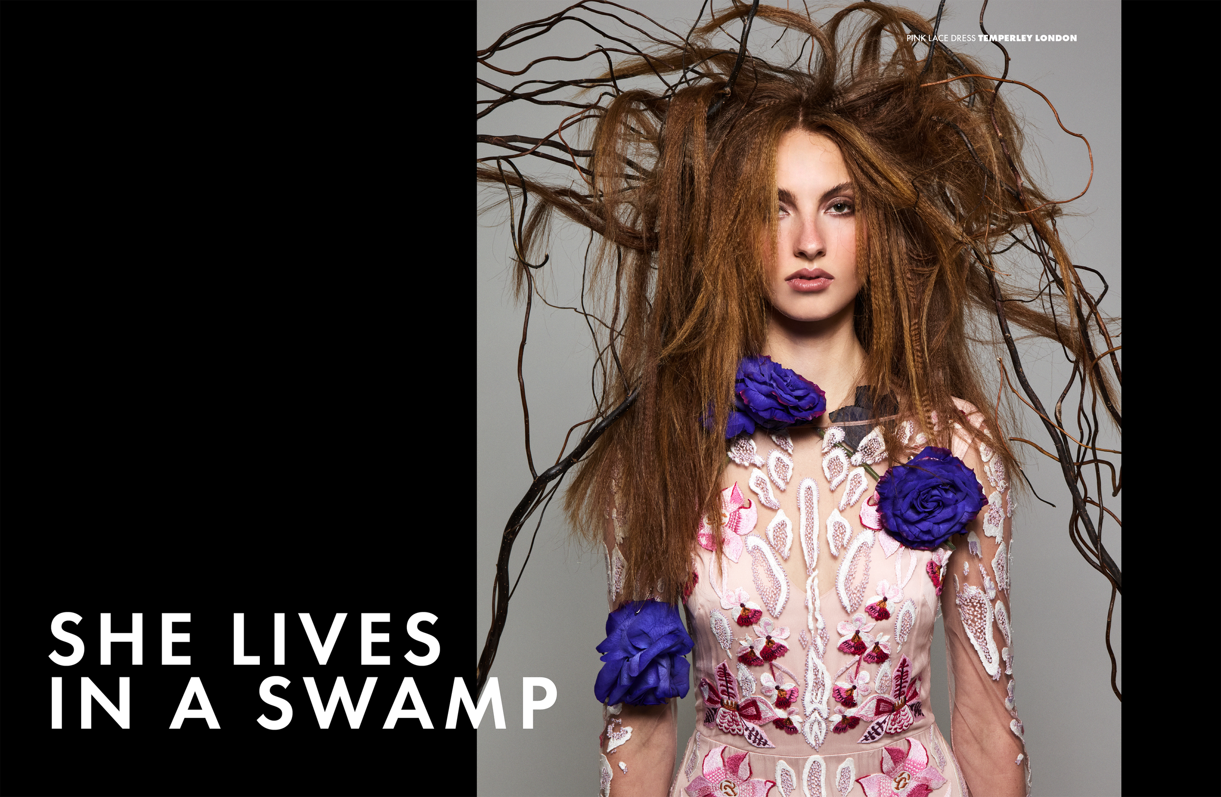 A woman with long, messy red hair wearing a sheer pink dress with white and pink floral embroidery. She has dark makeup and is decorated with large purple flowers on her dress and in her hair. Text in the image reads 'SHE LIVES IN A SWAMP,' and small text says 'PINK LACE DRESS TEMPERLEY LONDON.'