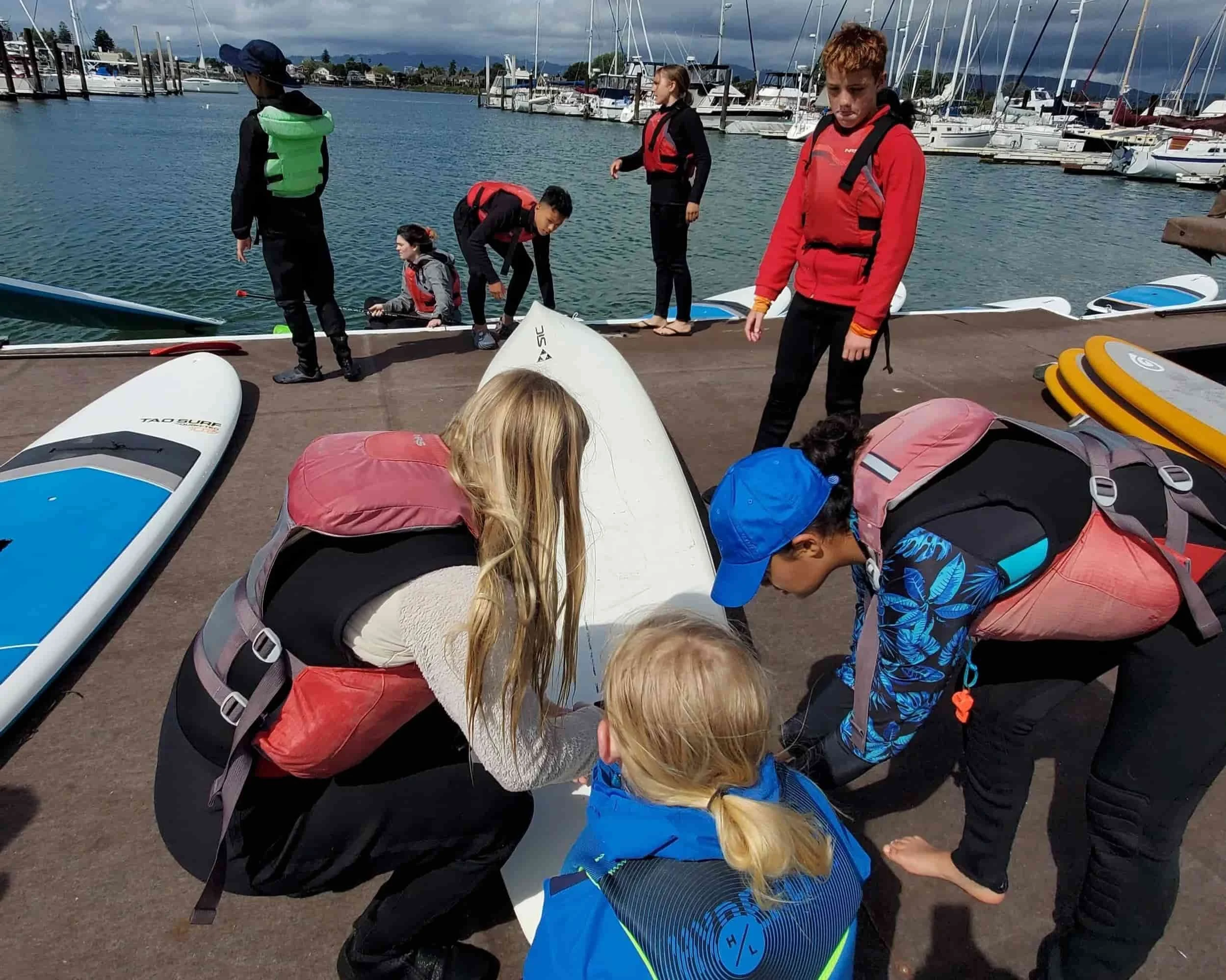 Children and adults preparing paddleboards at a marina, for our teen internship.