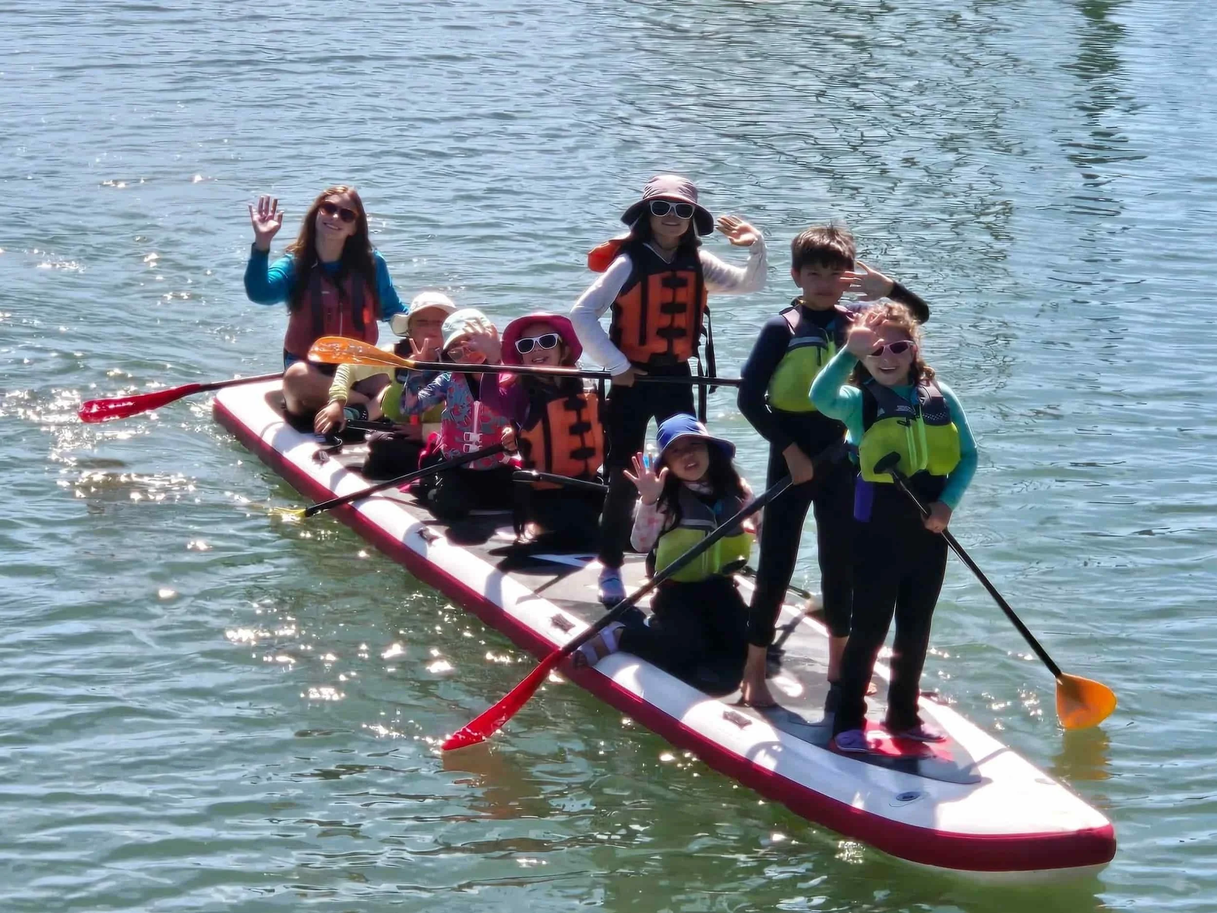 Children practicing teamwork on a big paddleboard for summer camp.
