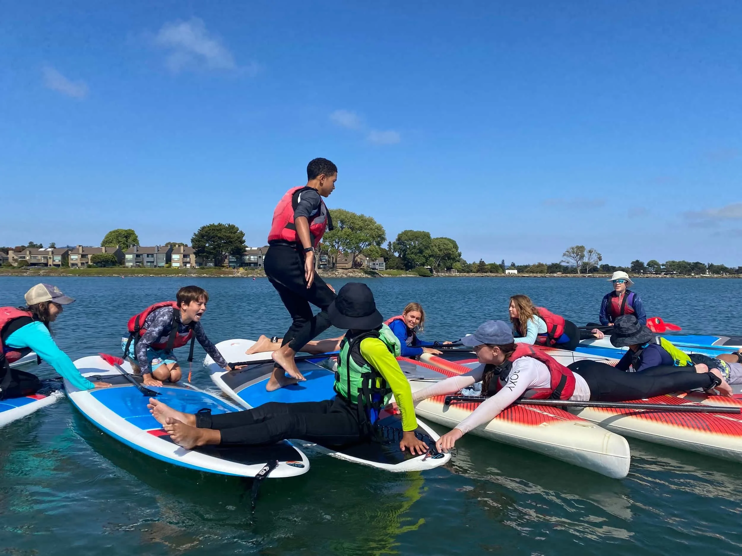 A group of children playing games on paddleboards and swimming at summer camp on Ballena Bay in Alameda.