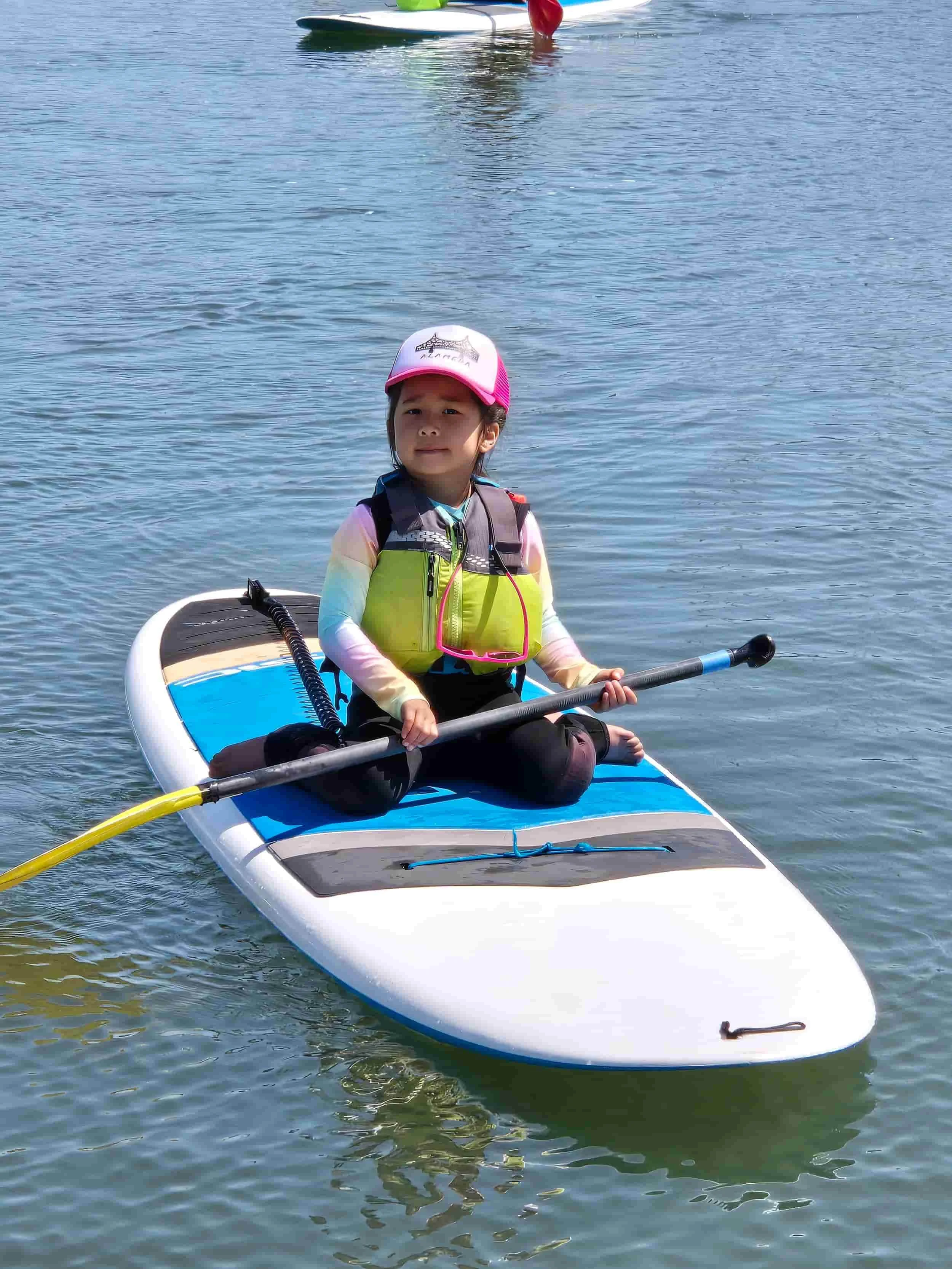 A young girl sitting on a paddleboard in adventure summer camp.