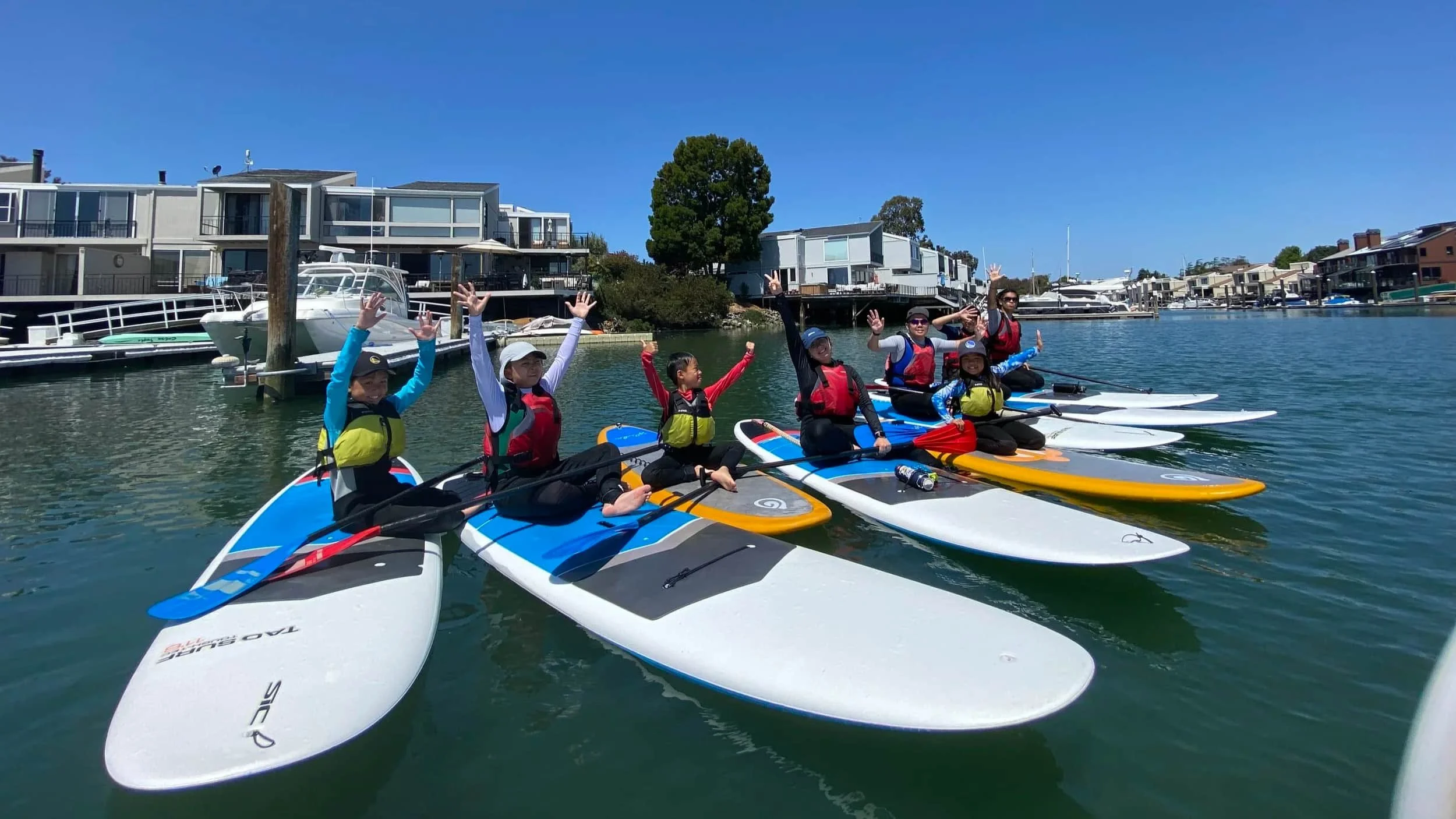 Family paddleboarding for Family Paddle Night on a calm waterway in Ballena Bay Marina in Alameda, California.