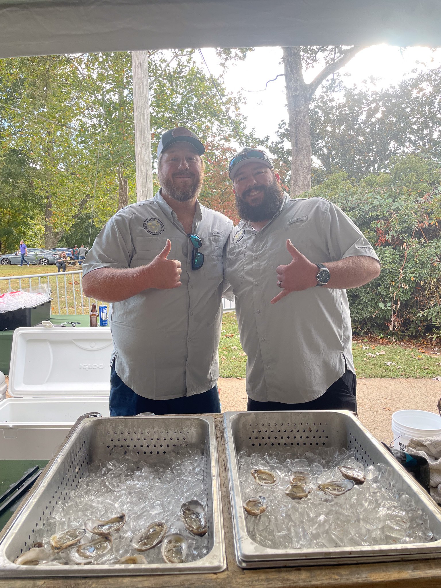  Two men giving a thumbs up beside an oyster display on ice outdoors 