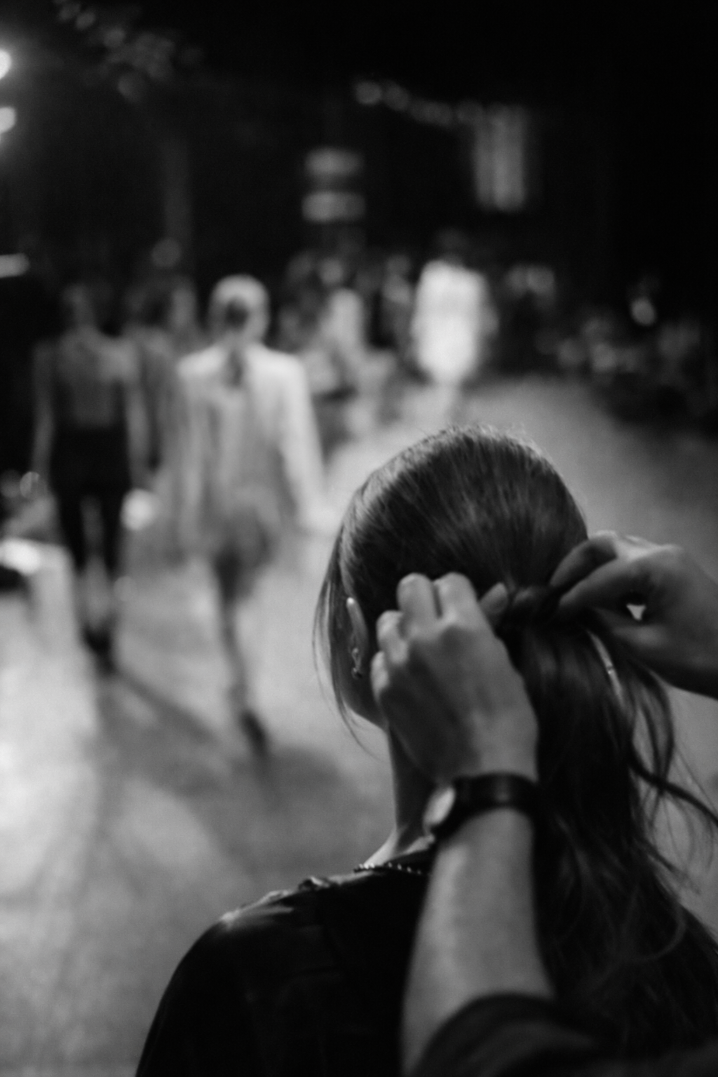 A person with long hair is getting their hair styled, with a crowd of people walking in the background on a city street at night.