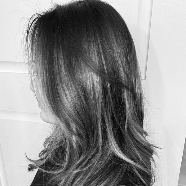 Woman with shoulder-length brown hair styled in loose waves, with blonde highlights, facing left against a white background.