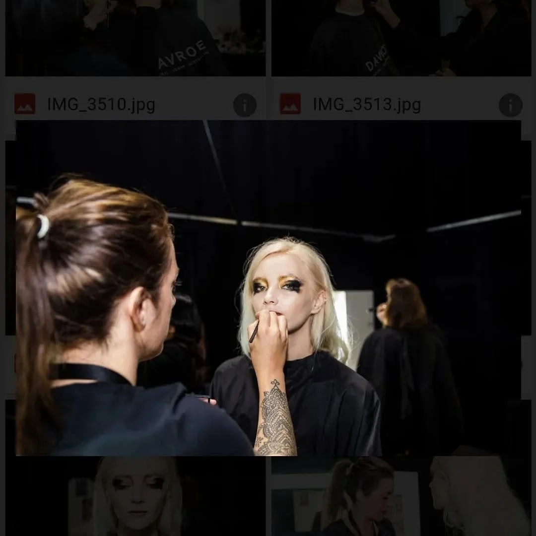 Makeup artist applies makeup to a blonde woman with dramatic eye makeup, in a black room with mirrors. Kaz ELizabeth NZ fashion week makeup and hair artist