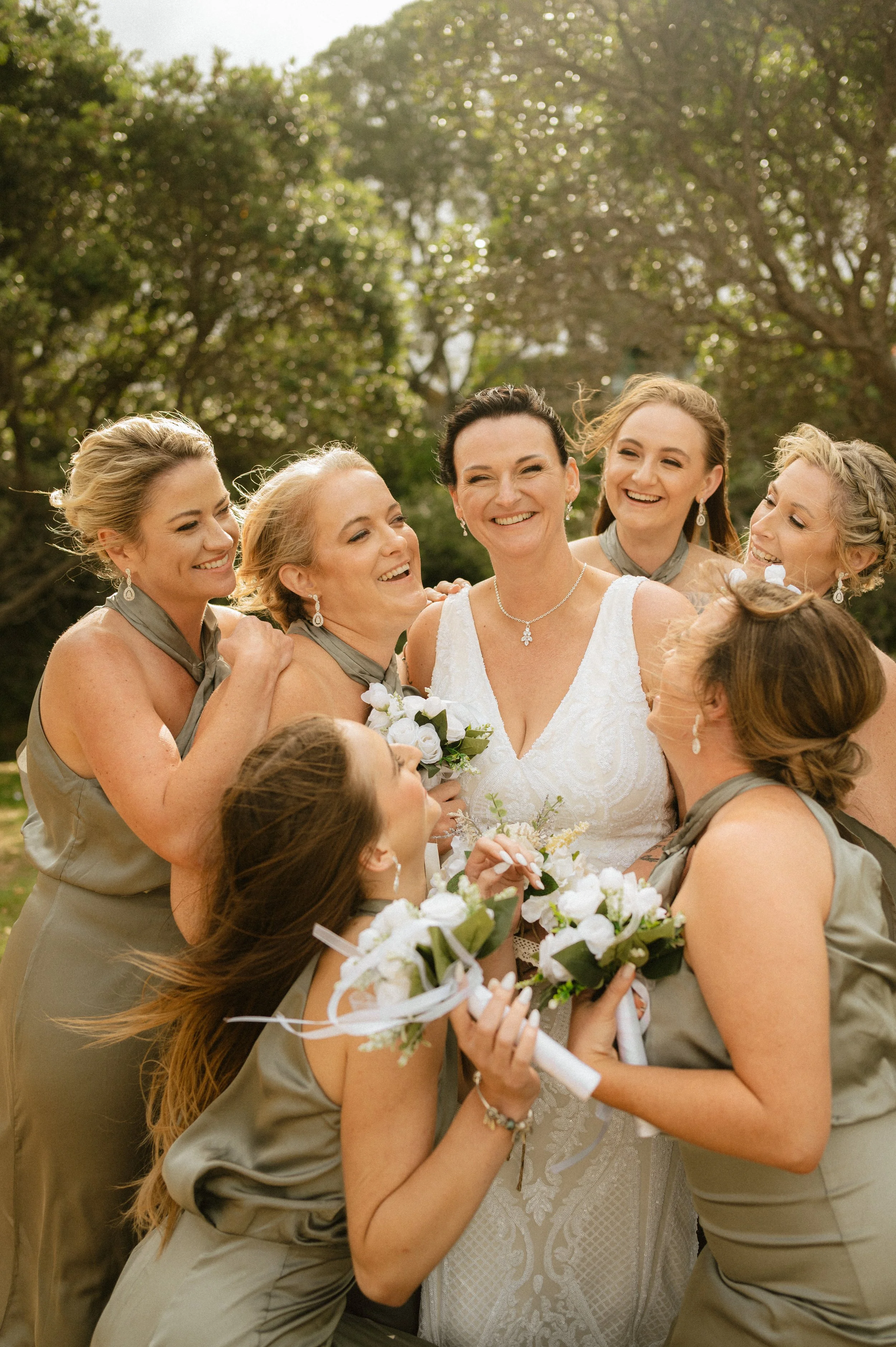 Bride laughing with bridesmaids while holding wedding flowers