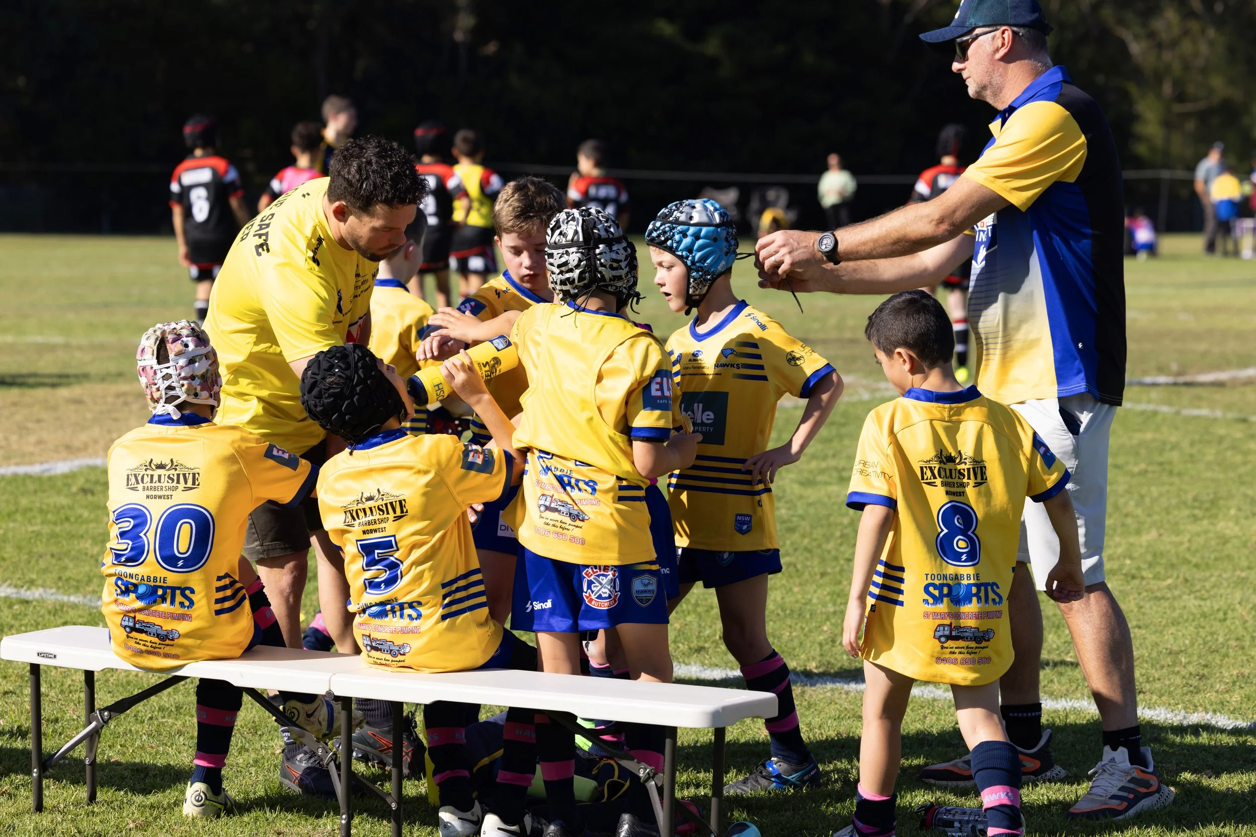Young rugby players in yellow jerseys listening to their coaches during a game.