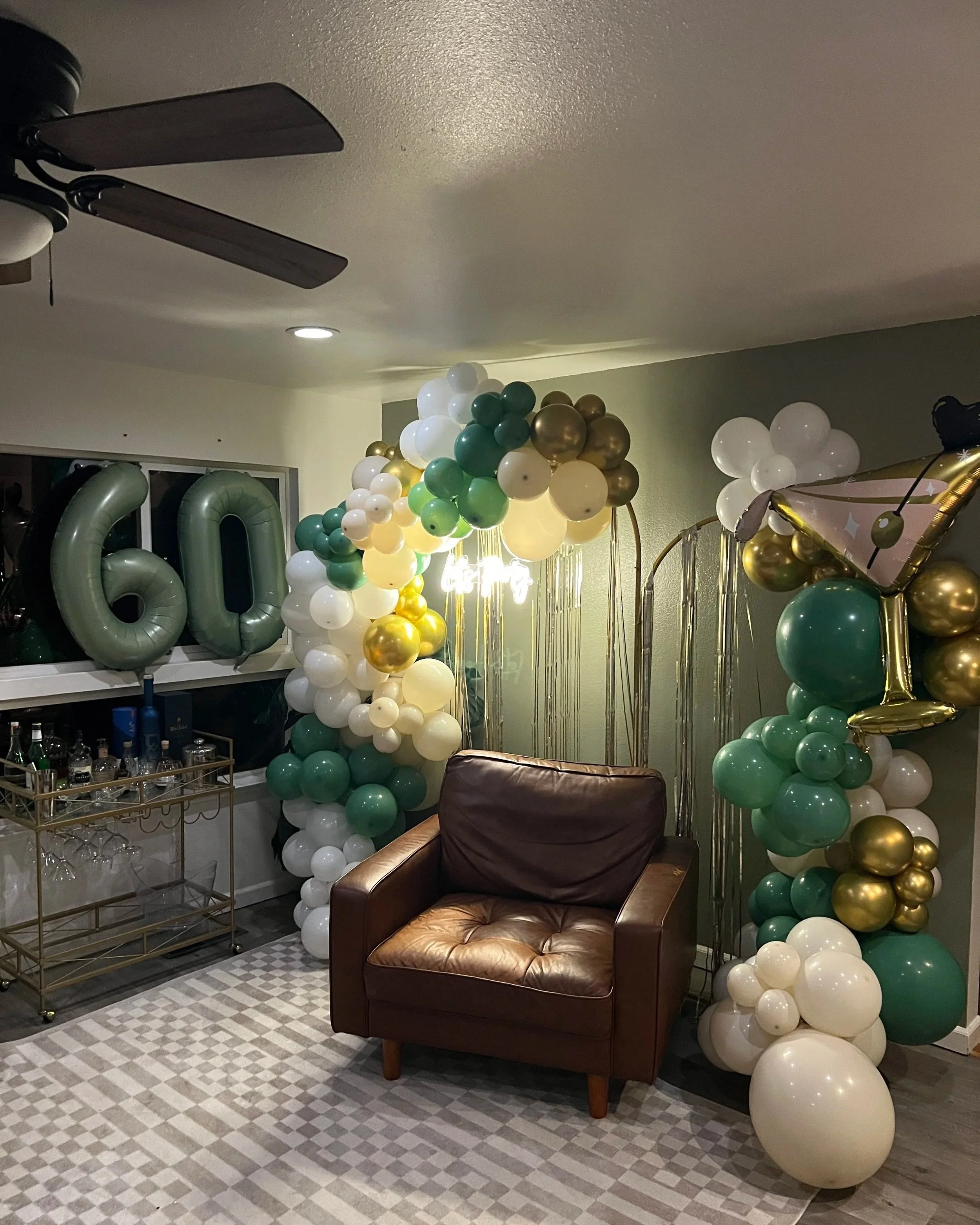 Decorative balloon arrangement for a 40th birthday celebration with gold, white, and green balloons, large gold '40' balloons, and a curtain backdrop.
