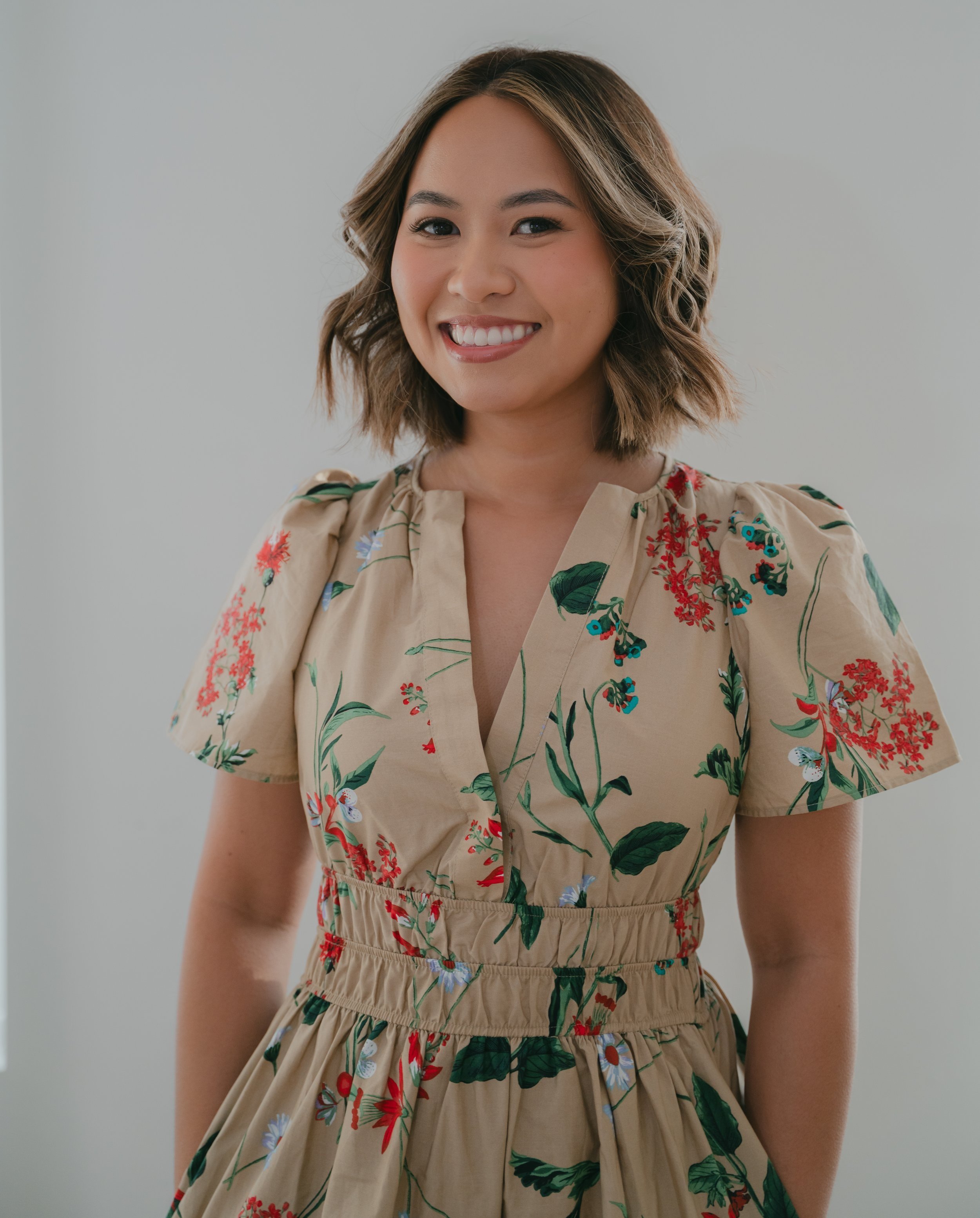 Smiling person with wavy hair wearing a floral dress.