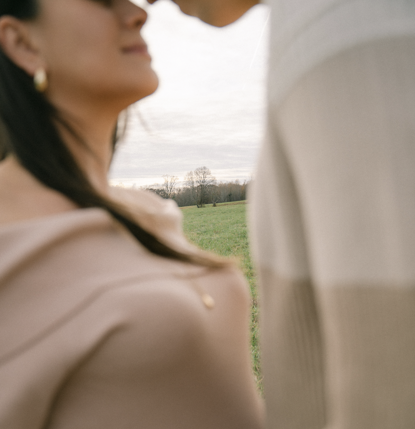 Close-up of two people facing each other in a grassy field, with a focus on the landscape in the background.
