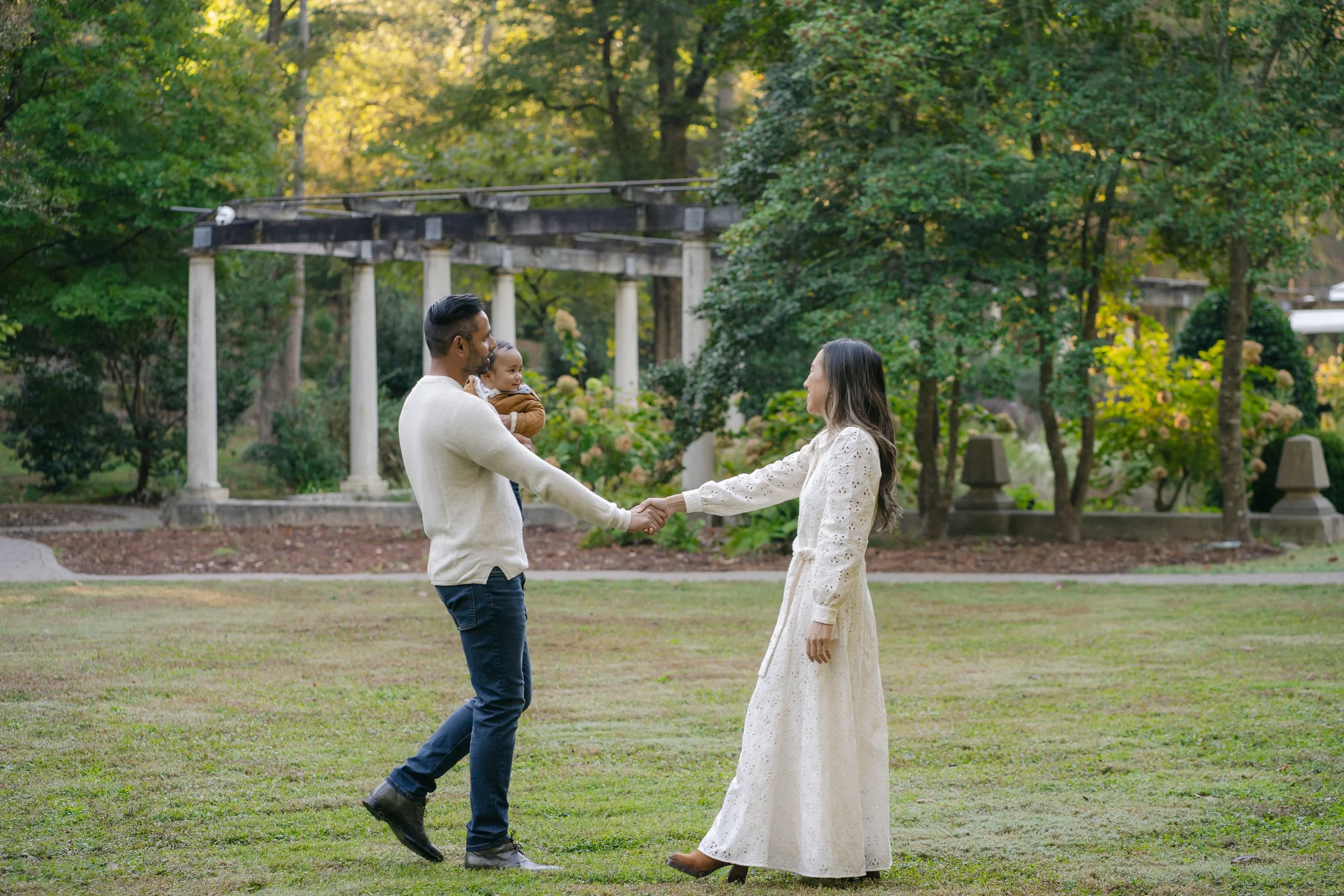 A couple with a baby in a park, with trees and columns in the background.