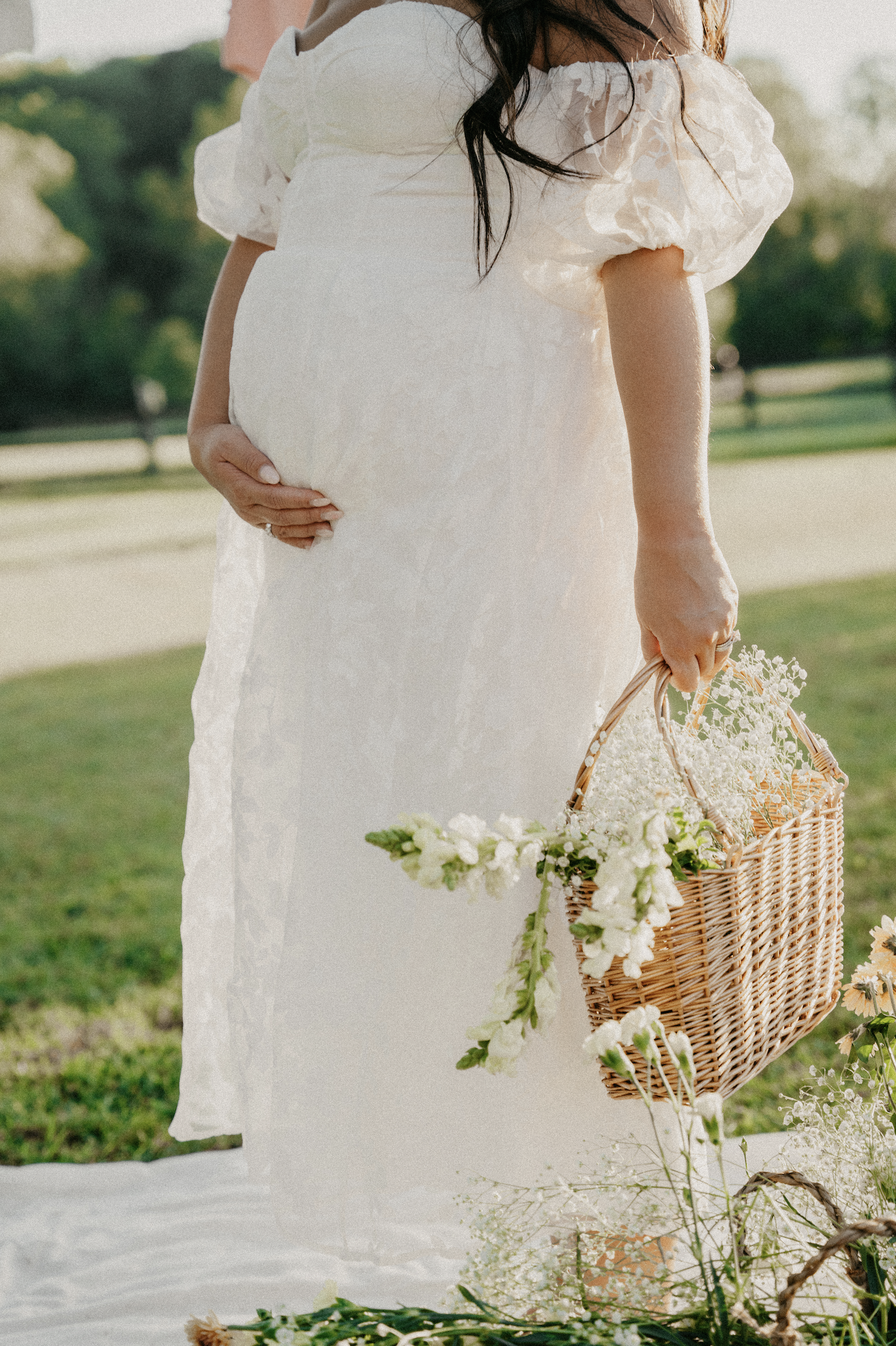 Pregnant woman in white dress holding basket of flowers outdoors