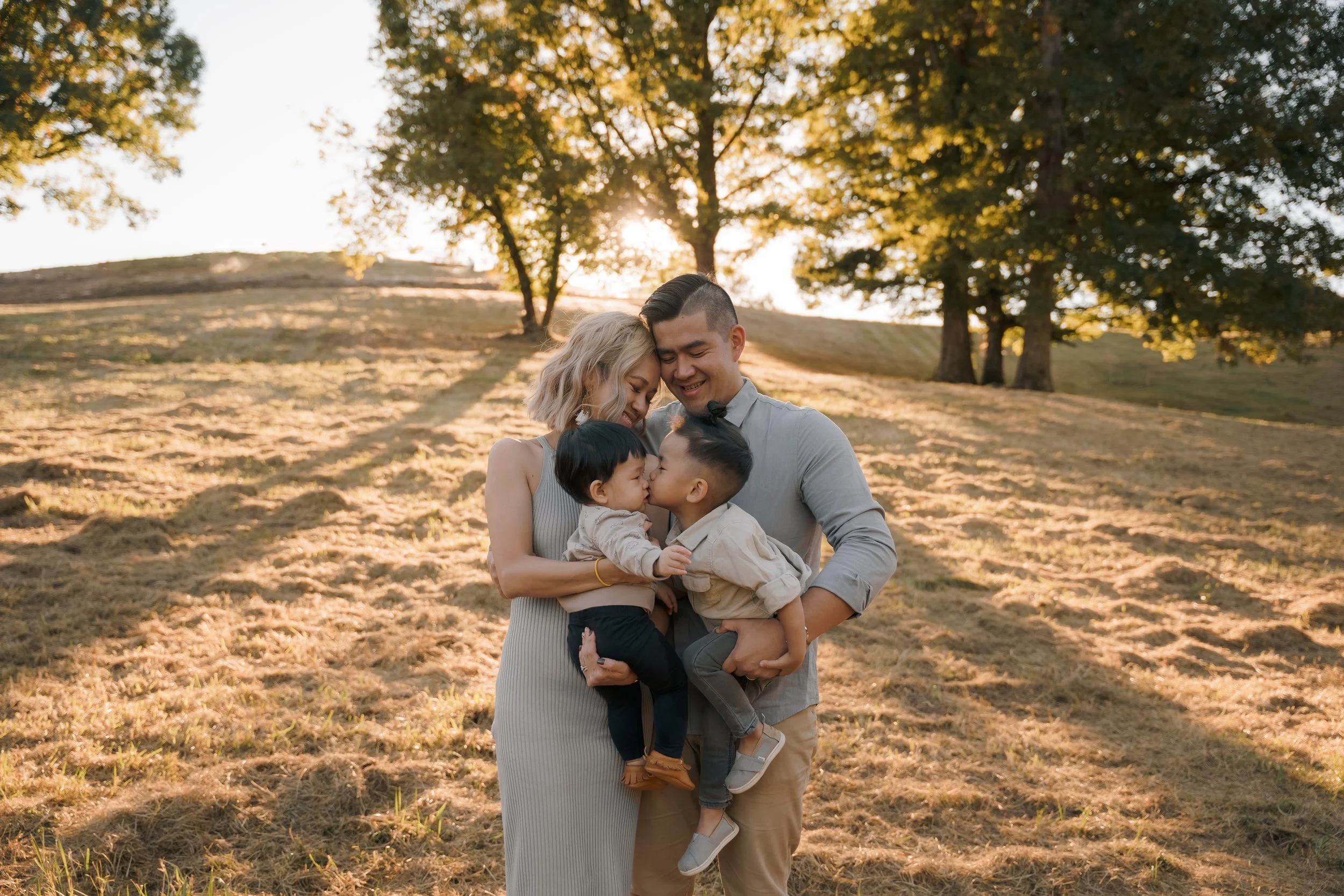Family hugging in a sunlit field with trees in the background.