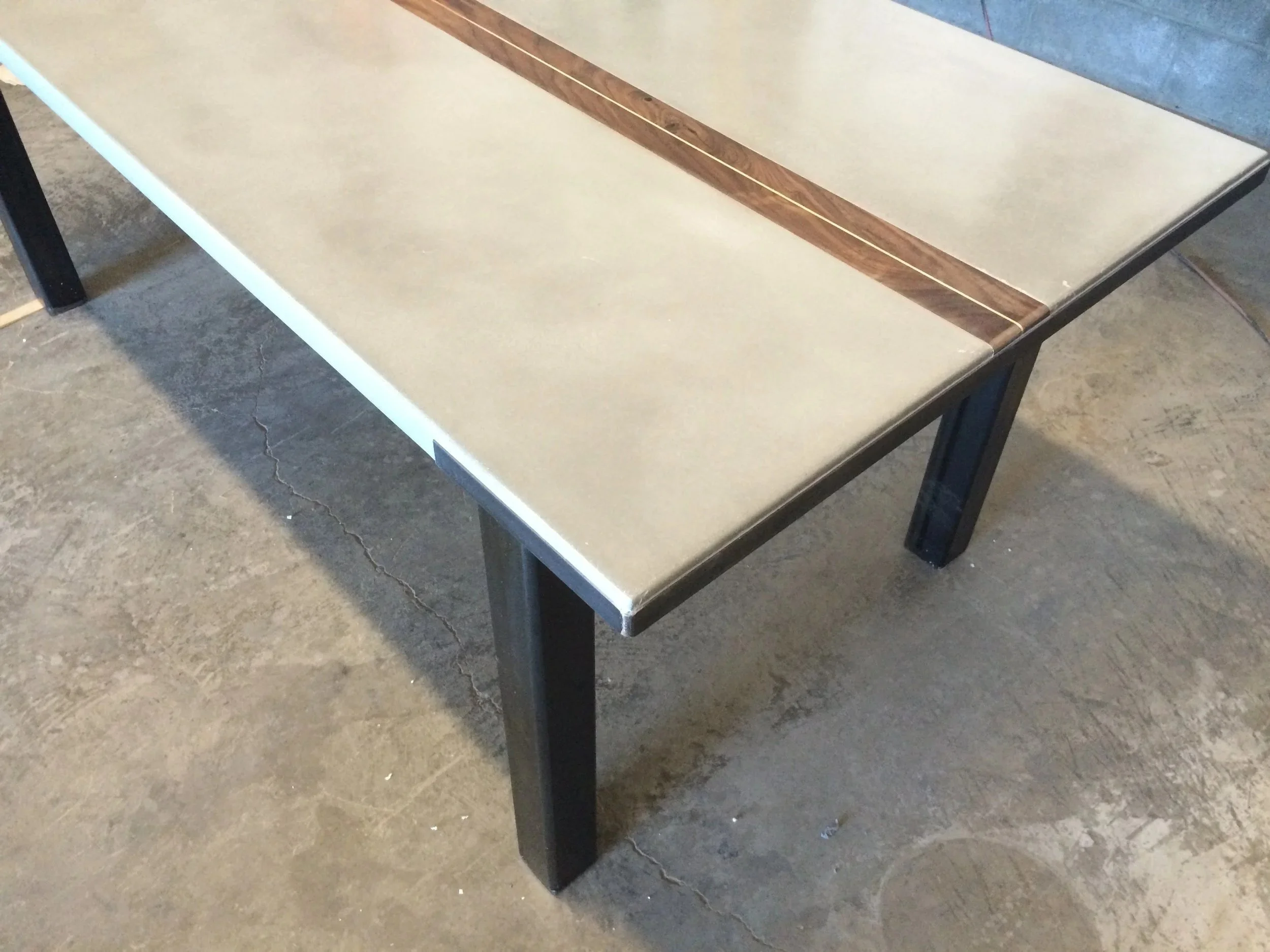 Handmade concrete dining table with walnut center inlay and steel edge detail with blackened steel base.