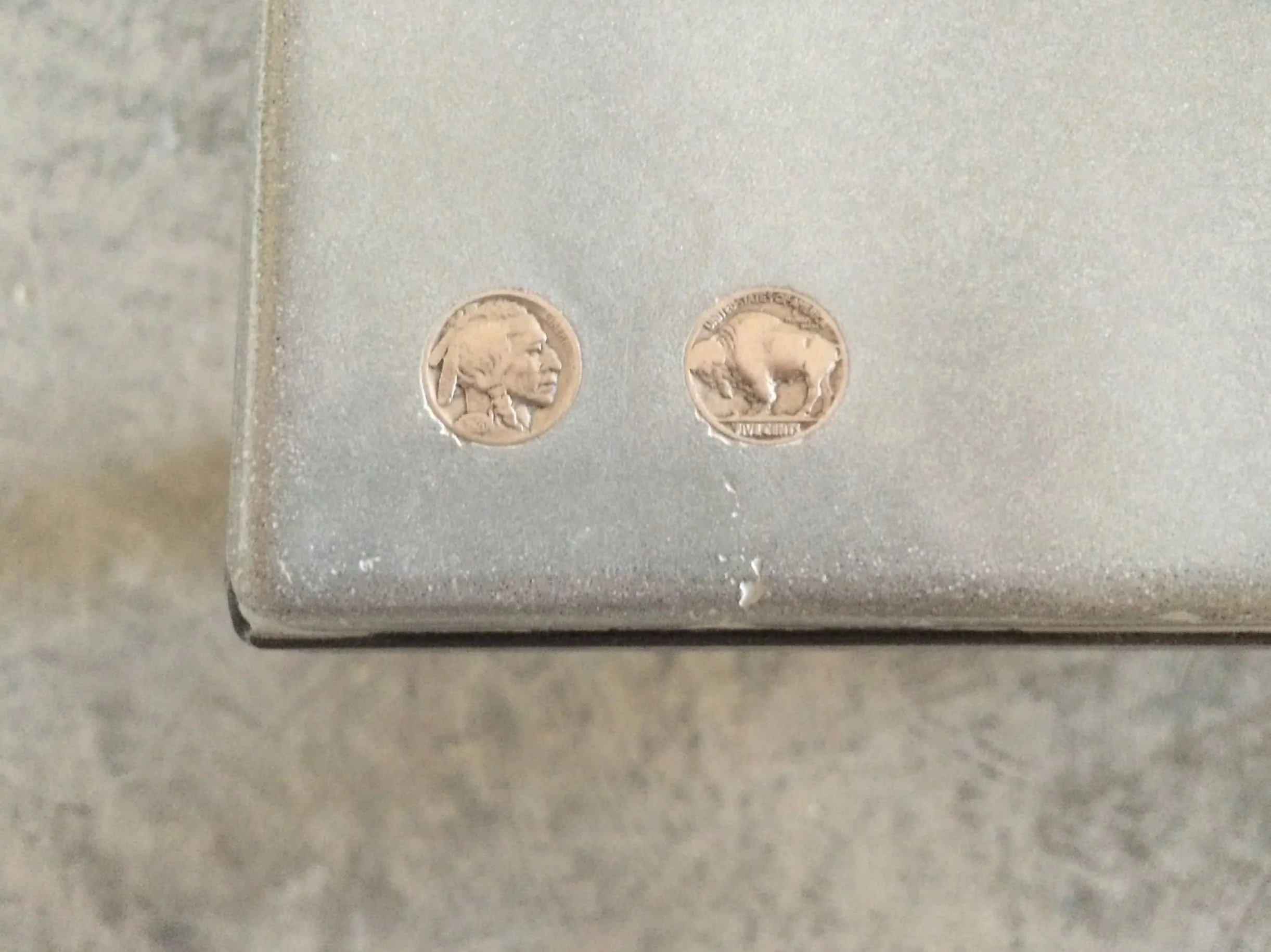 Head and tails, buffalo head nickels cast into concrete table corner.