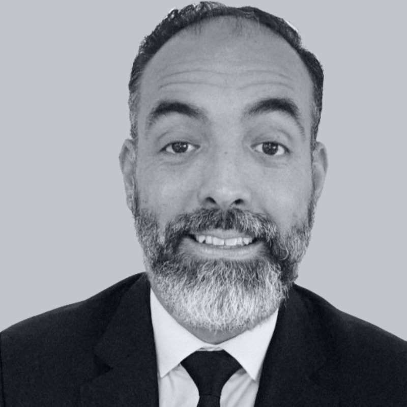 A smiling man with a beard and short hair, wearing a black collared shirt against a plain background.