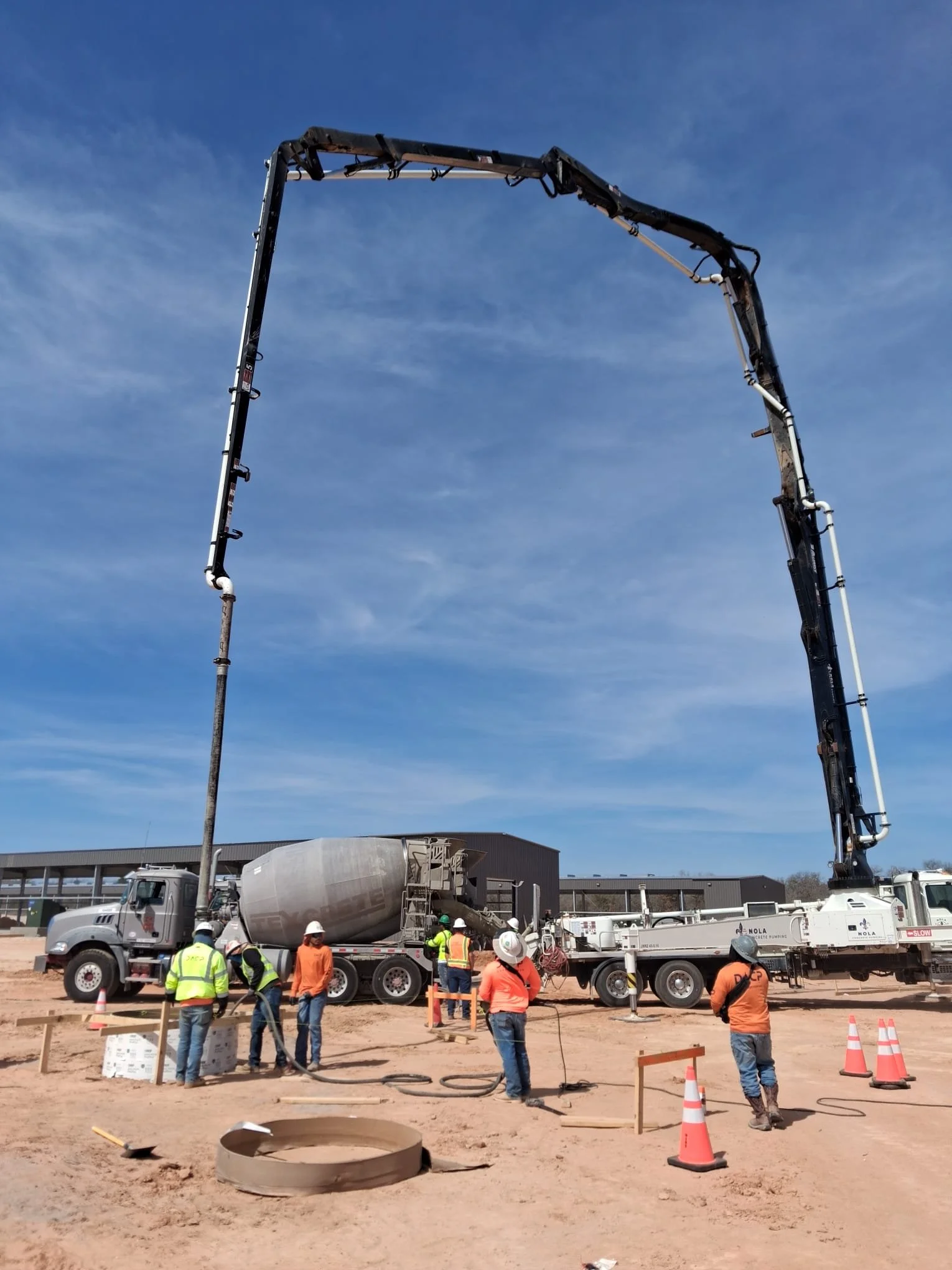 Construction workers operating a cement pump truck pouring concrete at a construction site.