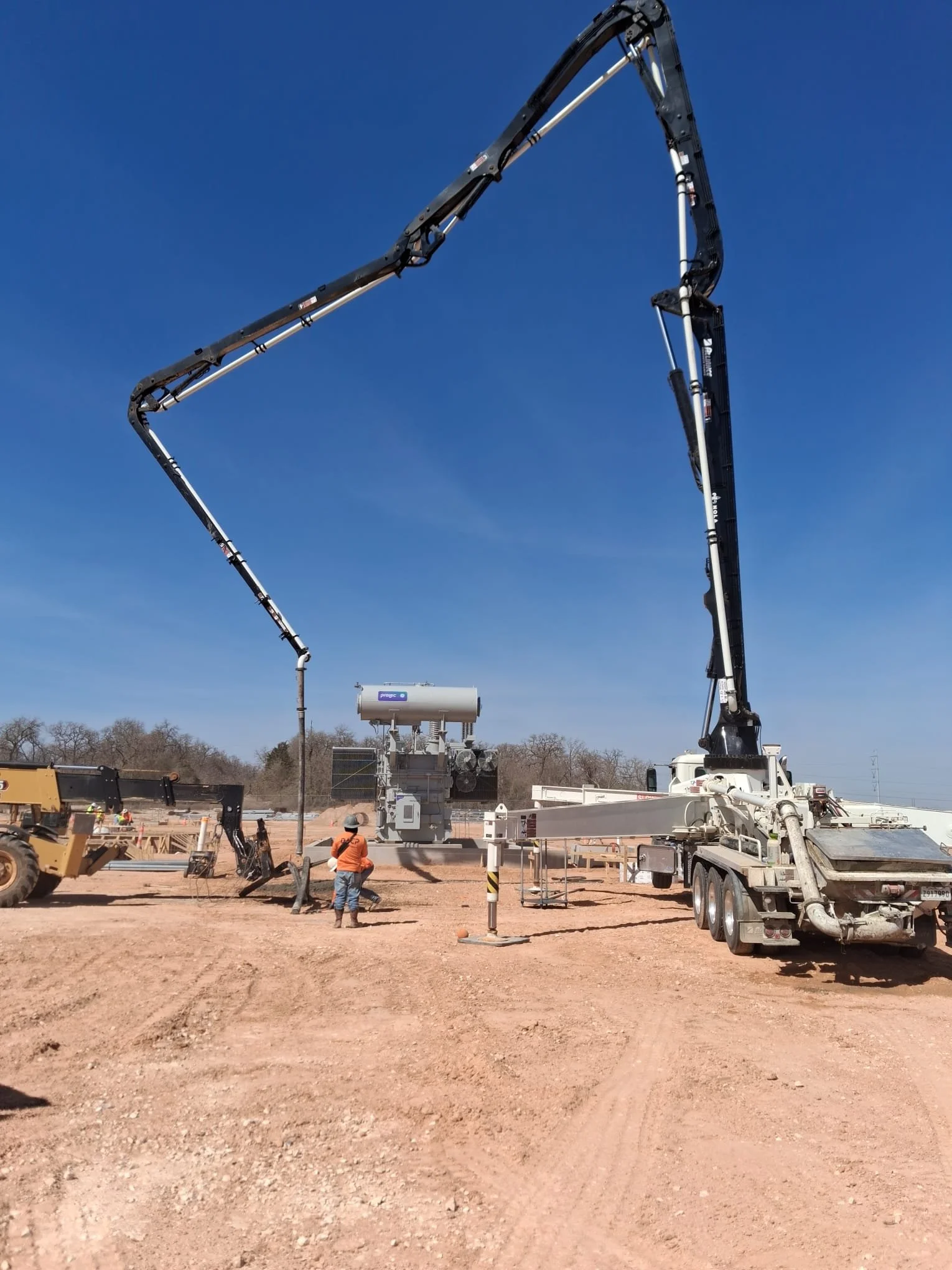 Construction workers operating a large concrete pump truck on a construction site with a clear blue sky.