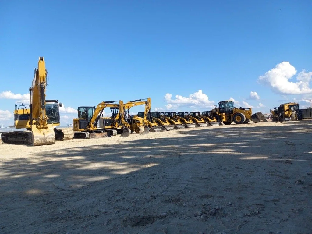 Three construction workers in yellow safety vests and helmets review blueprints and a laptop on a construction site.