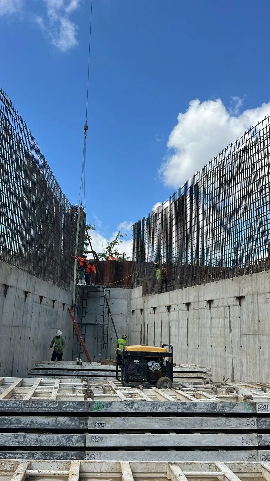 Workers paving a road with asphalt, using shovels and a paver, under a blue sky.