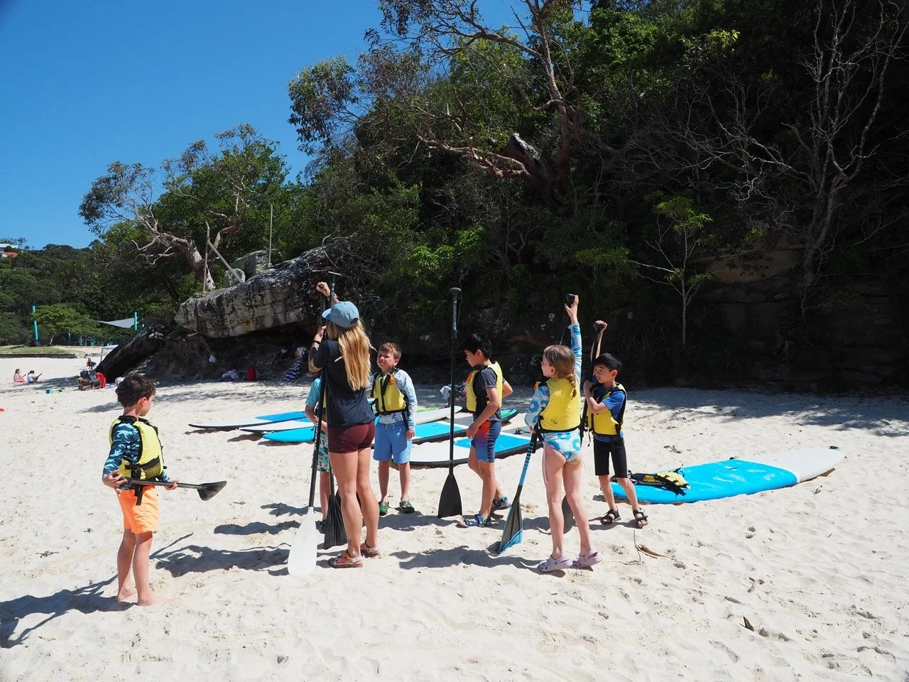 Group of children learning how to stand-up paddleboard with an instructor on the beach