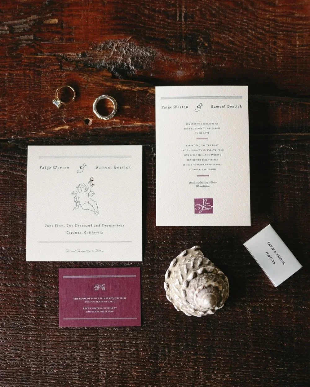 Wedding invitation suite with rings, a seashell, and RSVP card on a dark wooden surface.