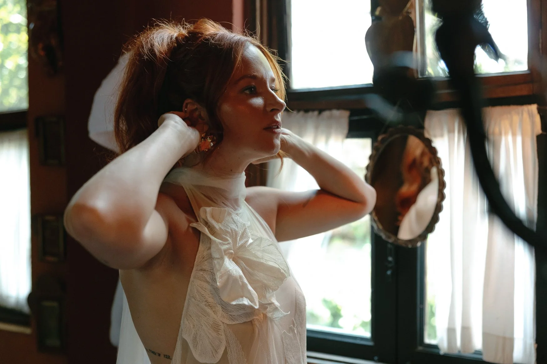 Woman adjusting her earrings in a white ruffled dress in front of a mirror in the bathroom of the bridal suite at casa hyder