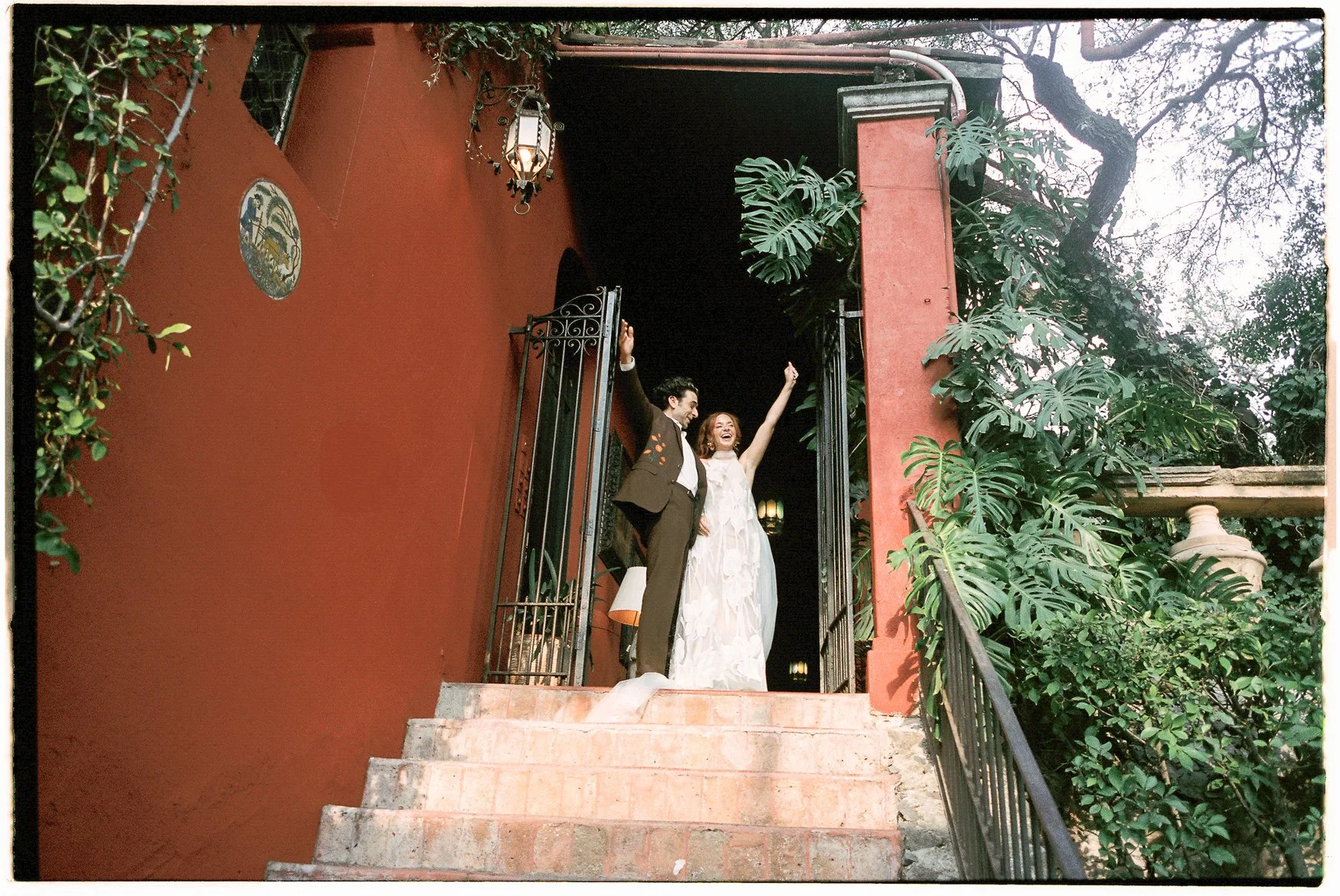Newlywed couple celebrating at the entrance of a Spanish-style home surrounded by lush greenery
