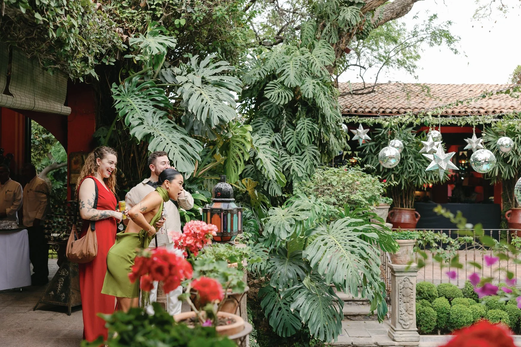 Guests socialize in a lush tropical courtyard decorated with hanging disco balls and star ornaments.