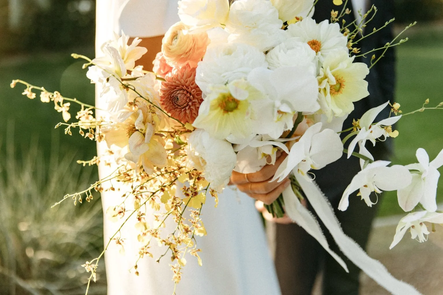 A person holding a bouquet of white, peach, and yellow flowers with green stems and leaves at the bougainvillea estate in palm springs