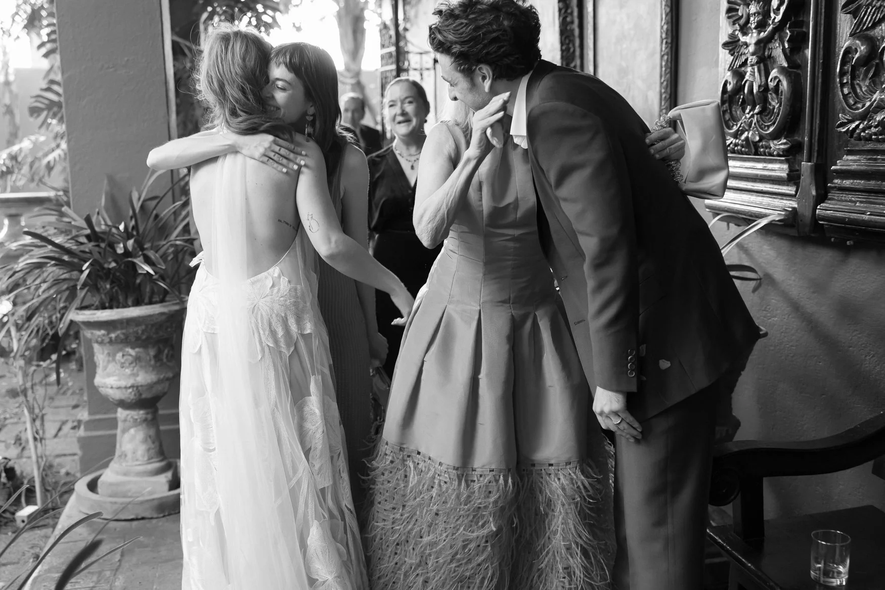 Black-and-white wedding reception scene with guests hugging and greeting one another in an elegant venue