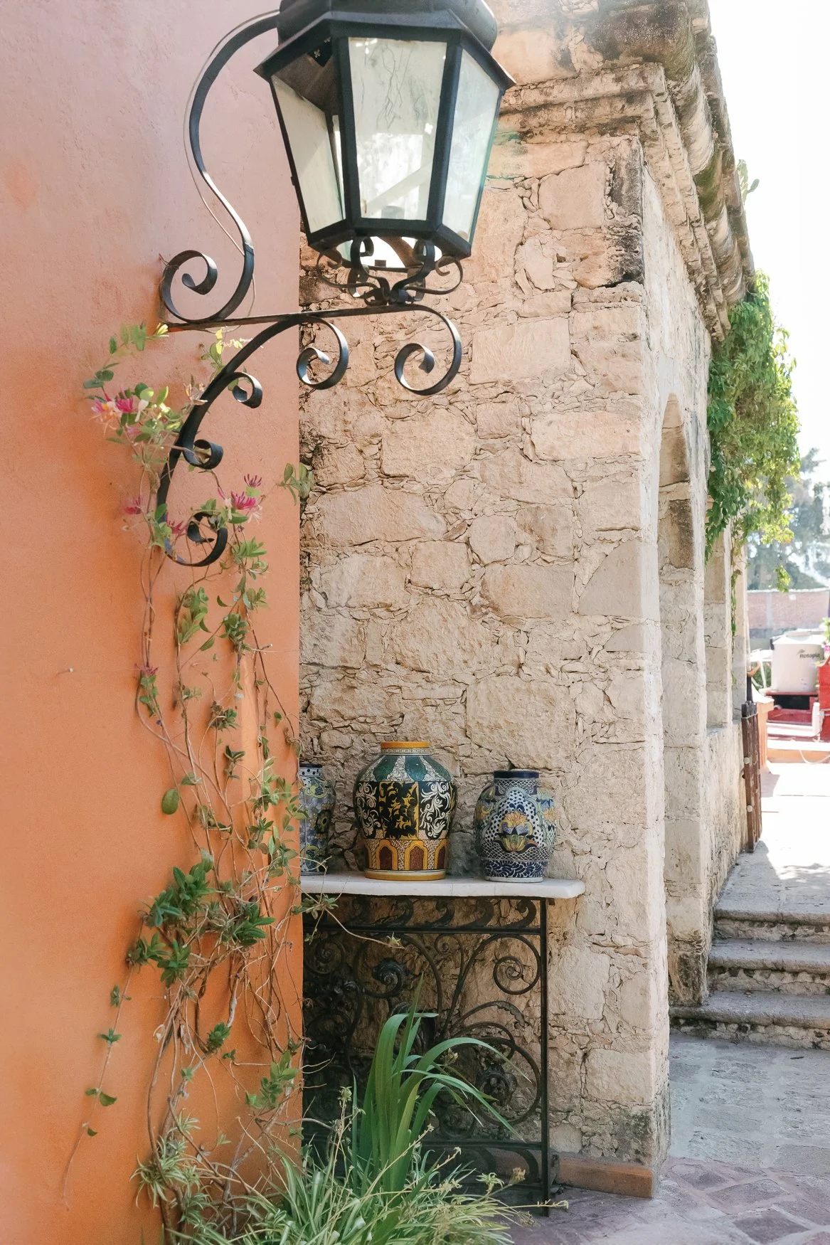 Decorative wrought-iron lantern beside colorful ceramic vases on a rustic stone wall with climbing plants