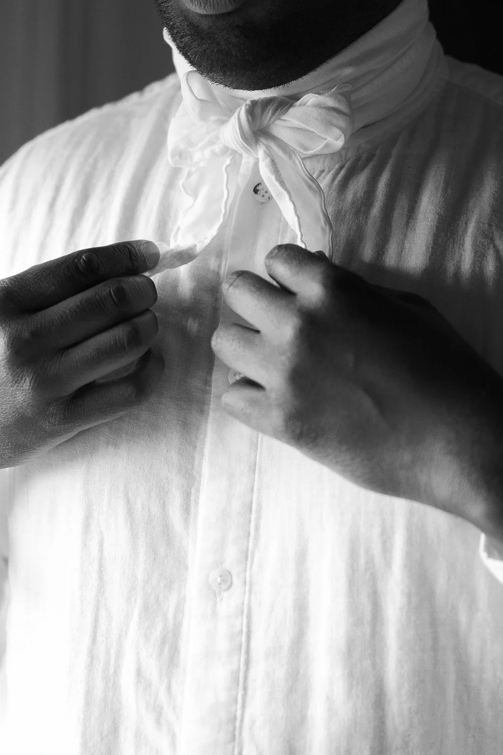 Close-up black and white photo of a man adjusting his white dress shirt collar and tie, with a small ladybug on the collar.