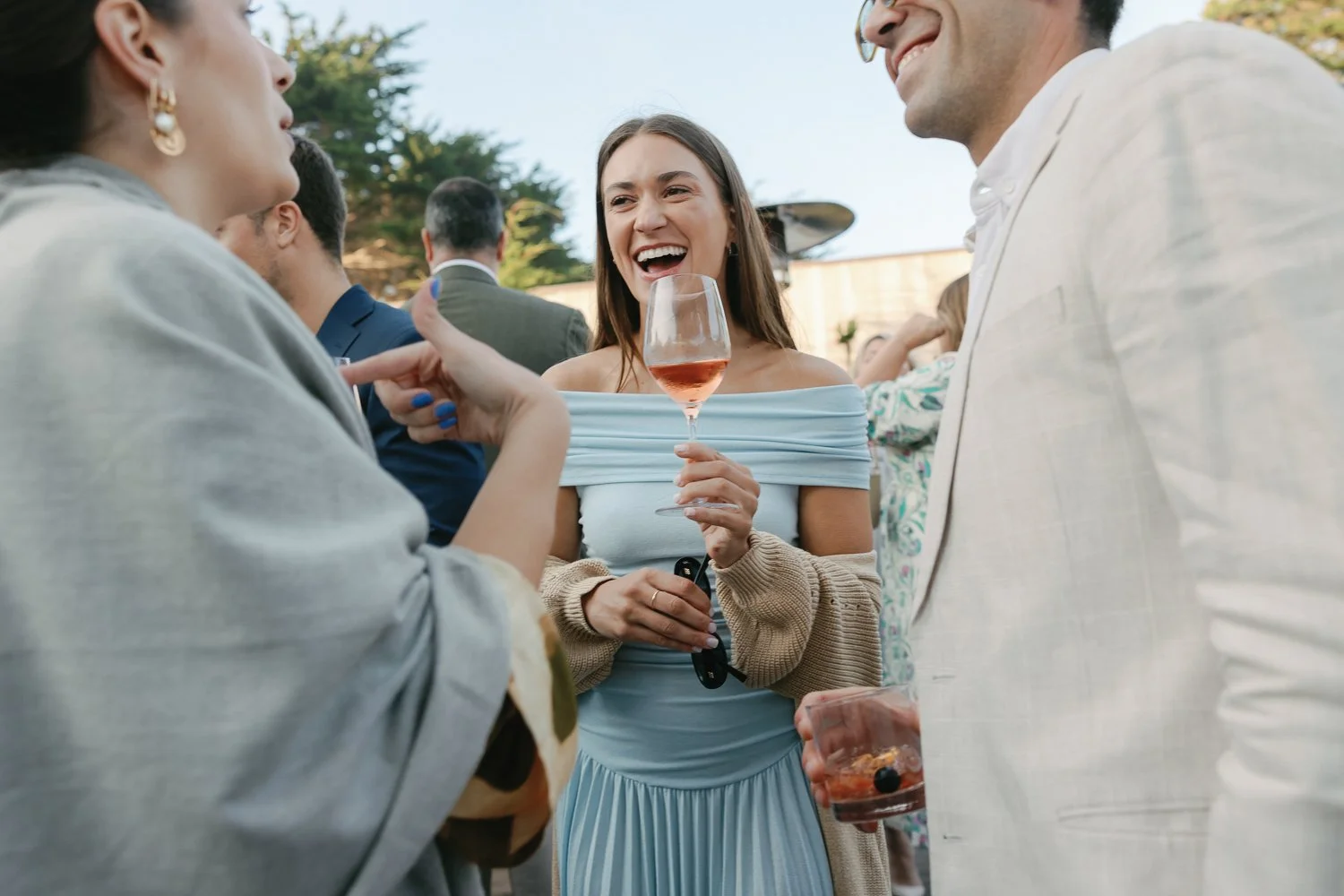 People socializing outdoors, smiling, and holding drinks at a gathering during a welcome party on the Deck at the sea ranch lodge