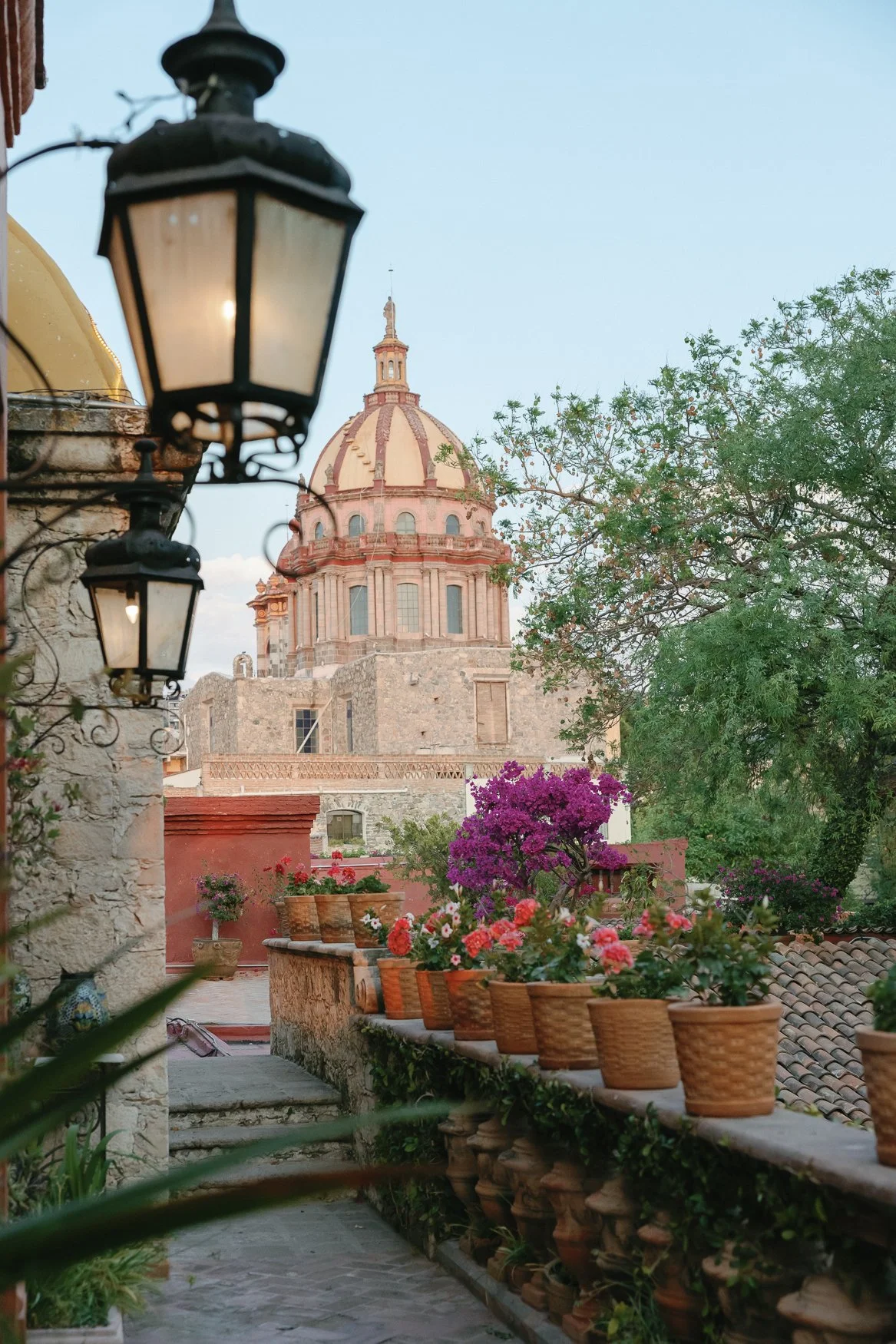 Colonial courtyard garden with potted flowers, lanterns, and a historic domed church in the background in san miguel de allende