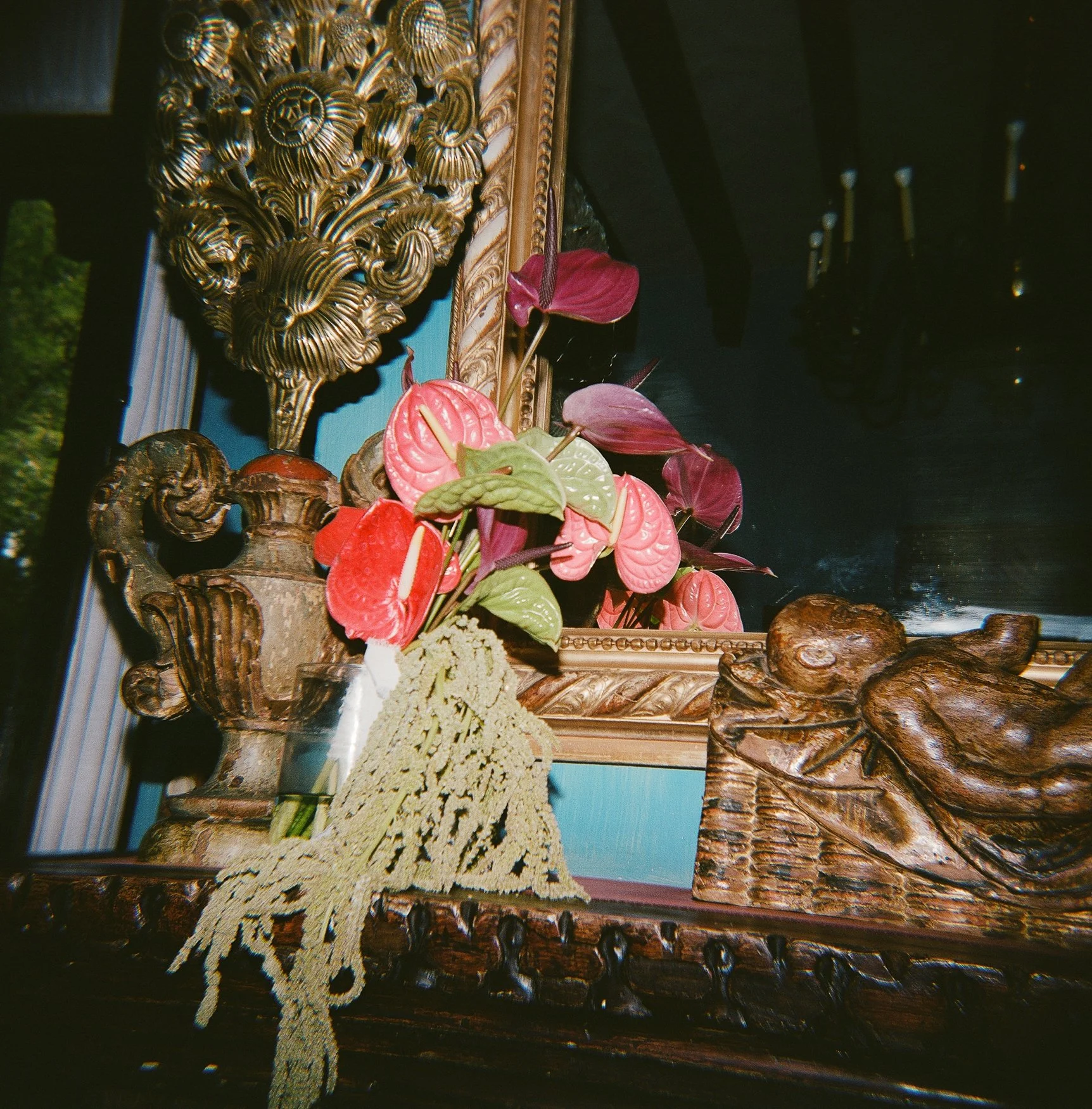 Ornate gold-framed mirror and carved wooden furniture decorated with colorful anthurium flowers and greenery