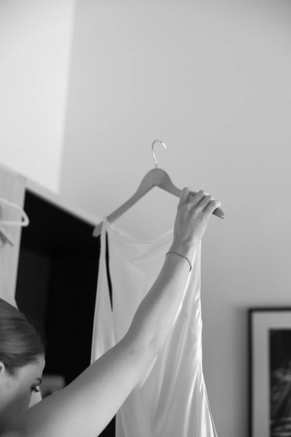 Woman hanging a white dress on a wooden hanger in a room.