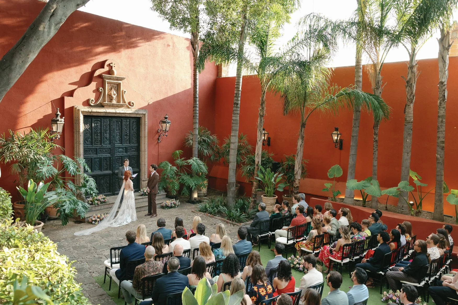 Outdoor wedding ceremony in a lush courtyard with the bride and groom at an ornate doorway and seated guests at casa hyder